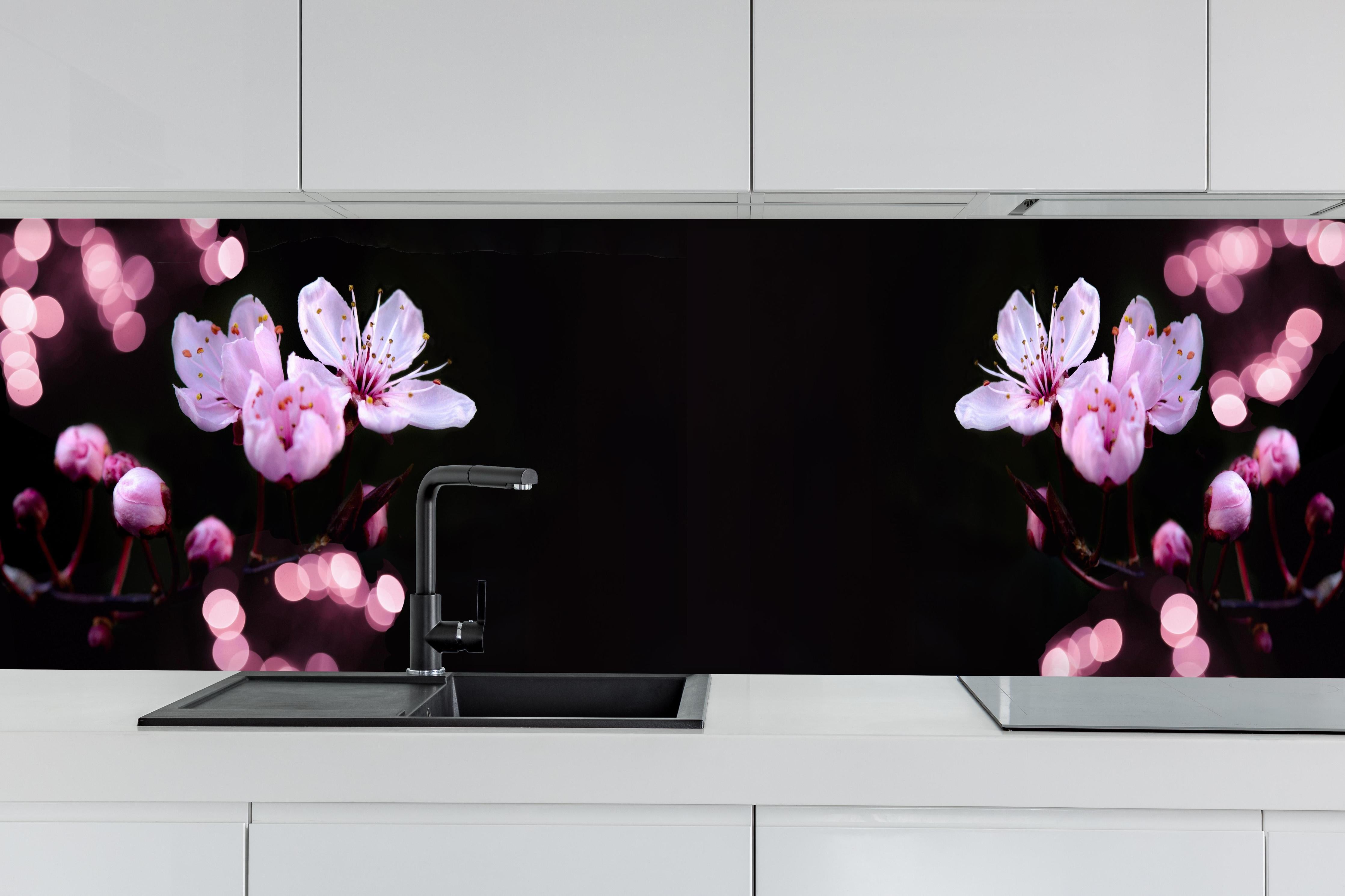 Küche - Zarte Rosa Kirschblüten beleuchtet in Dunkelheit hinter weißen Hochglanz-Küchenregalen und schwarzem Wasserhahn