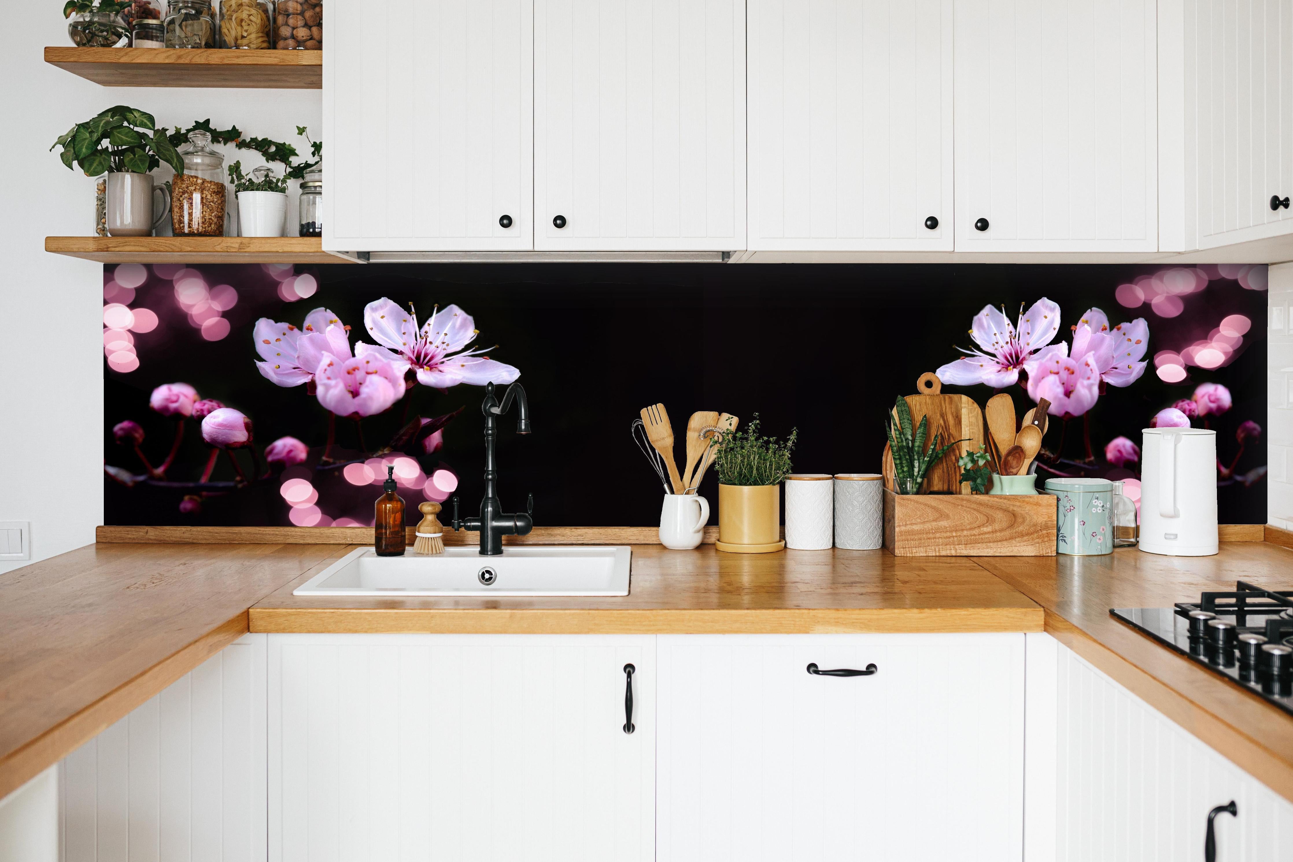 Küche - Zarte Rosa Kirschblüten beleuchtet in Dunkelheit hinter weißen Hochglanz-Küchenregalen und schwarzem Wasserhahn
