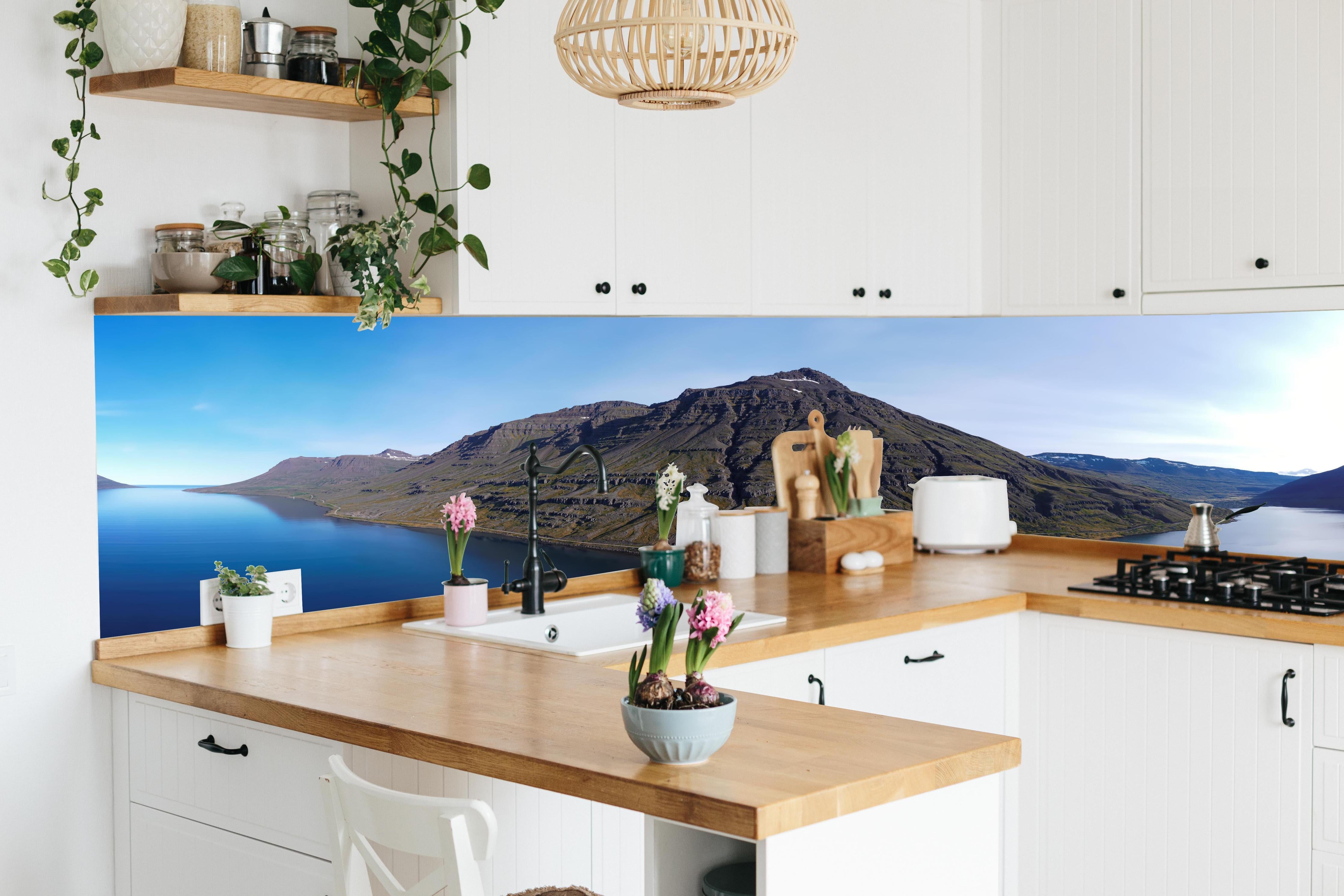 Küche - luftbildpanorama in den isländischen ostfjorden hinter weißen Hochglanz-Küchenregalen und schwarzem Wasserhahn