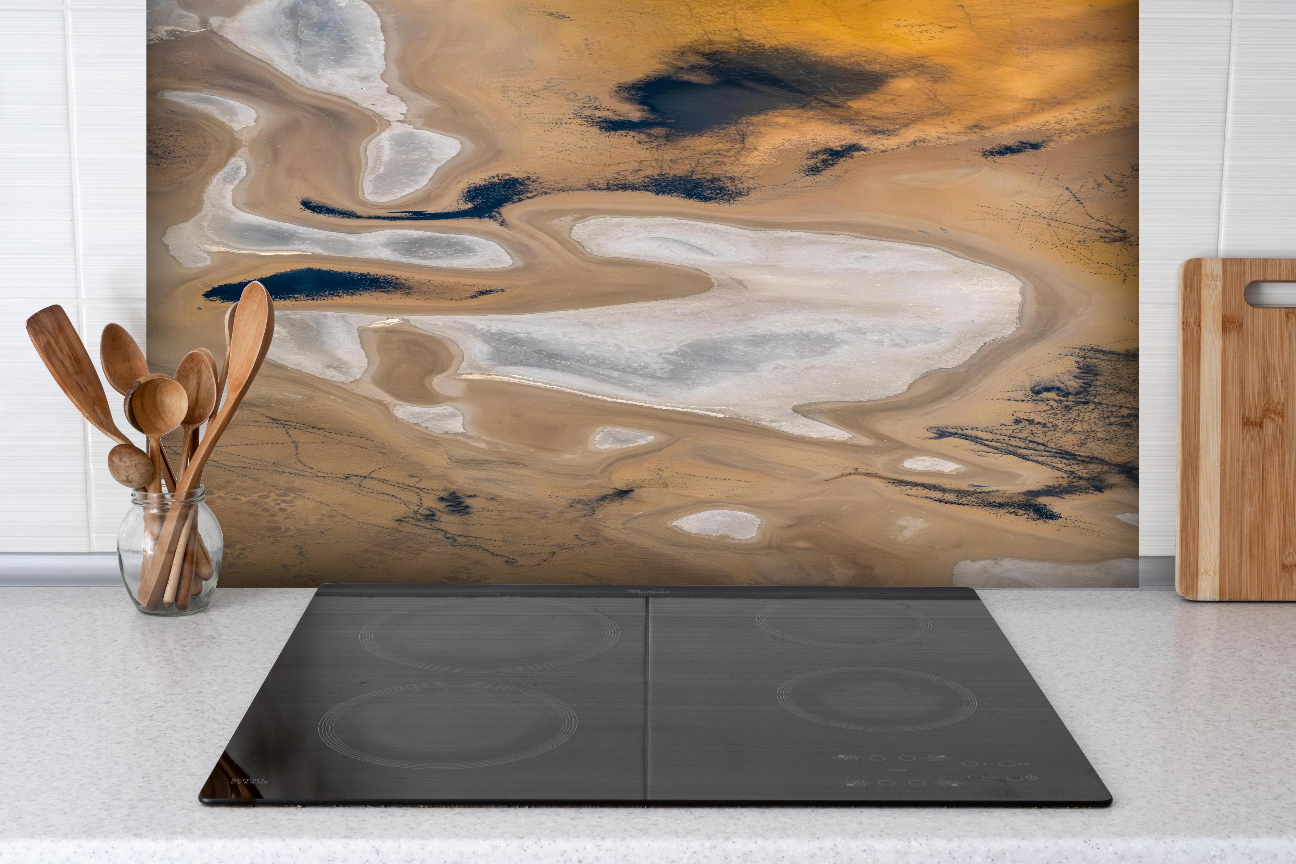 Spritzschutz - Abstrakte Landschaft in Beige-Tönen hinter einem Cerankochfeld zwischen Holz-Kochutensilien