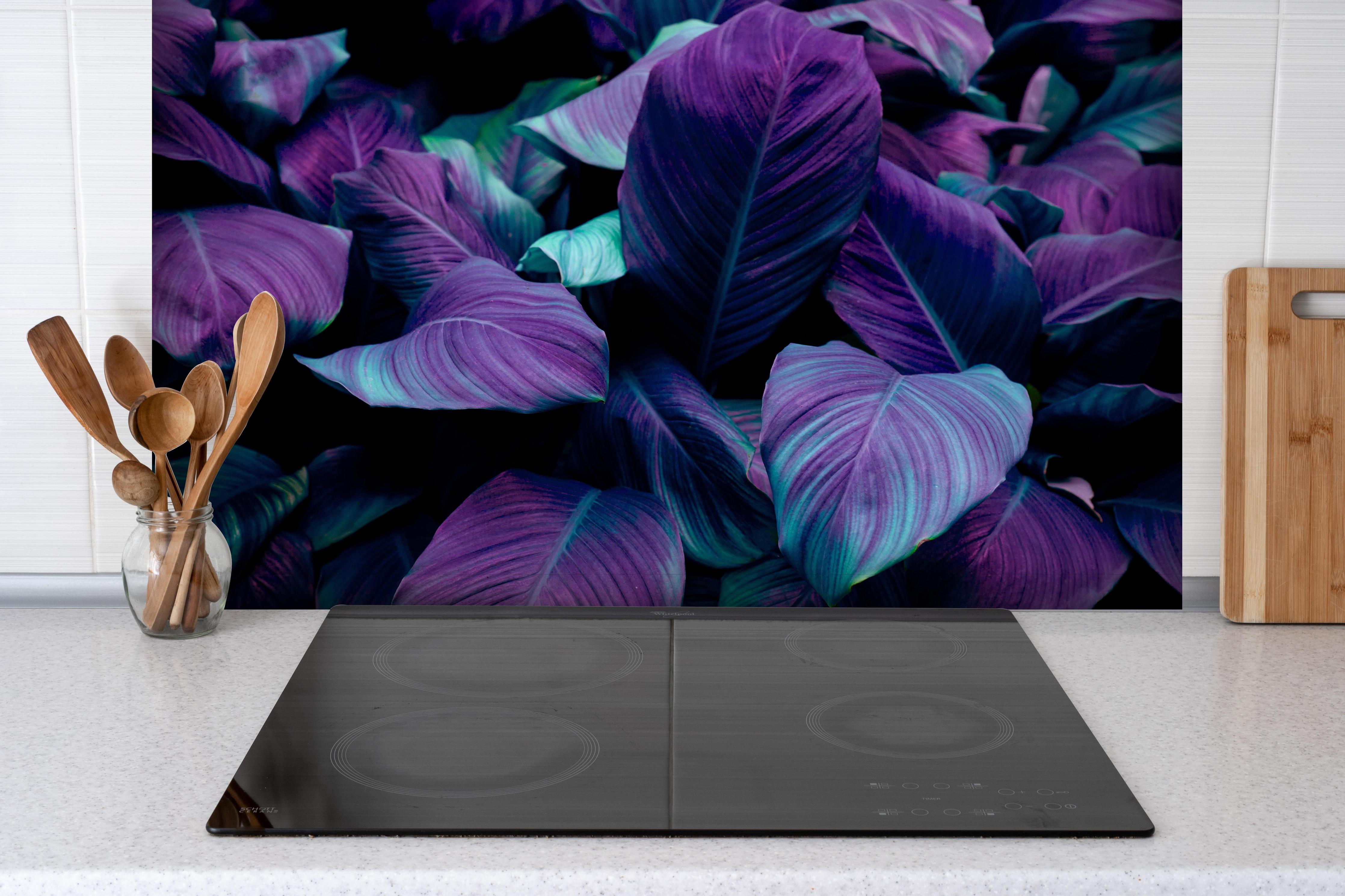 Spritzschutz - Abstrakte Tropenblätter in dunklen Farbtönen hinter einem Cerankochfeld zwischen Holz-Kochutensilien