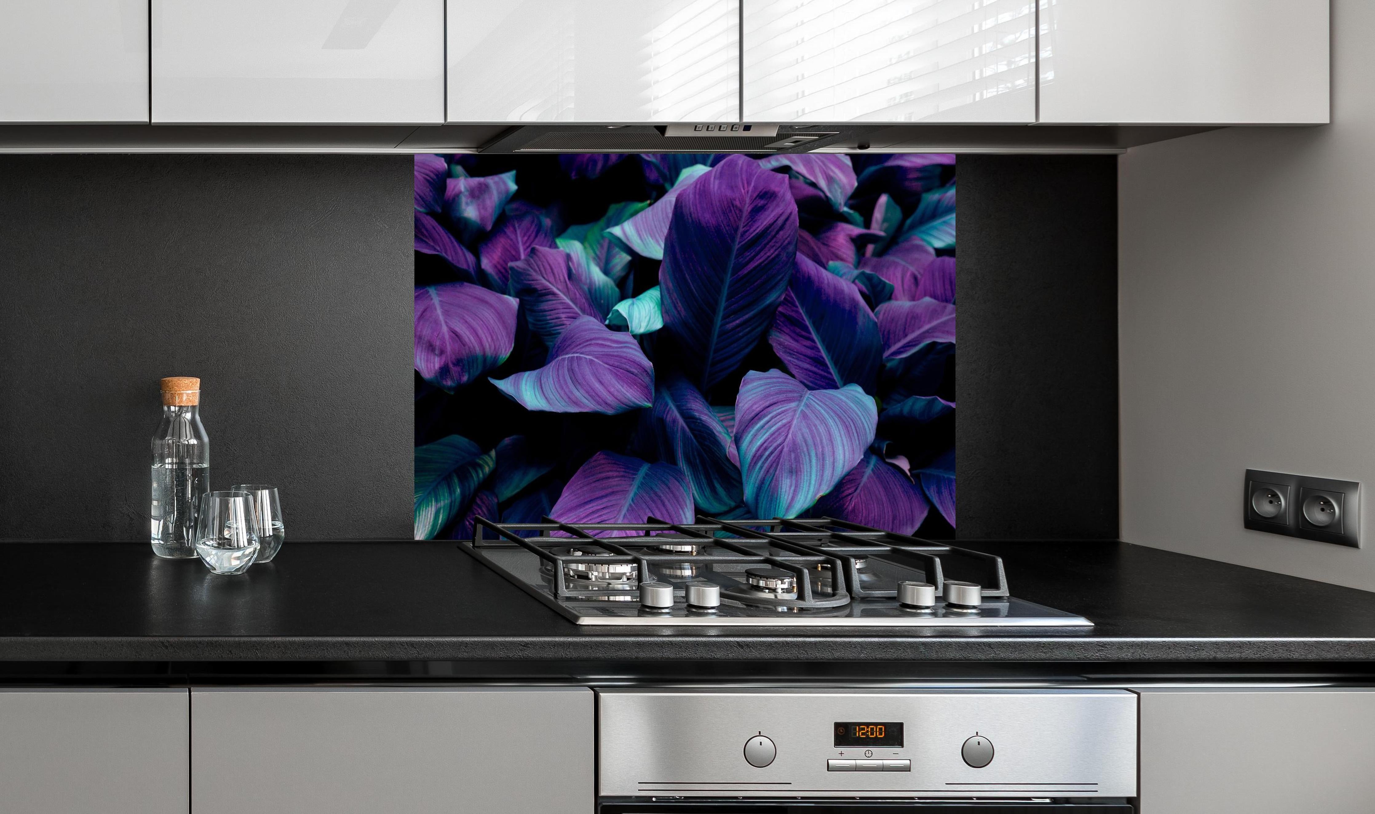 Spritzschutz - Abstrakte Tropenblätter in dunklen Farbtönen hinter einem Cerankochfeld zwischen Holz-Kochutensilien