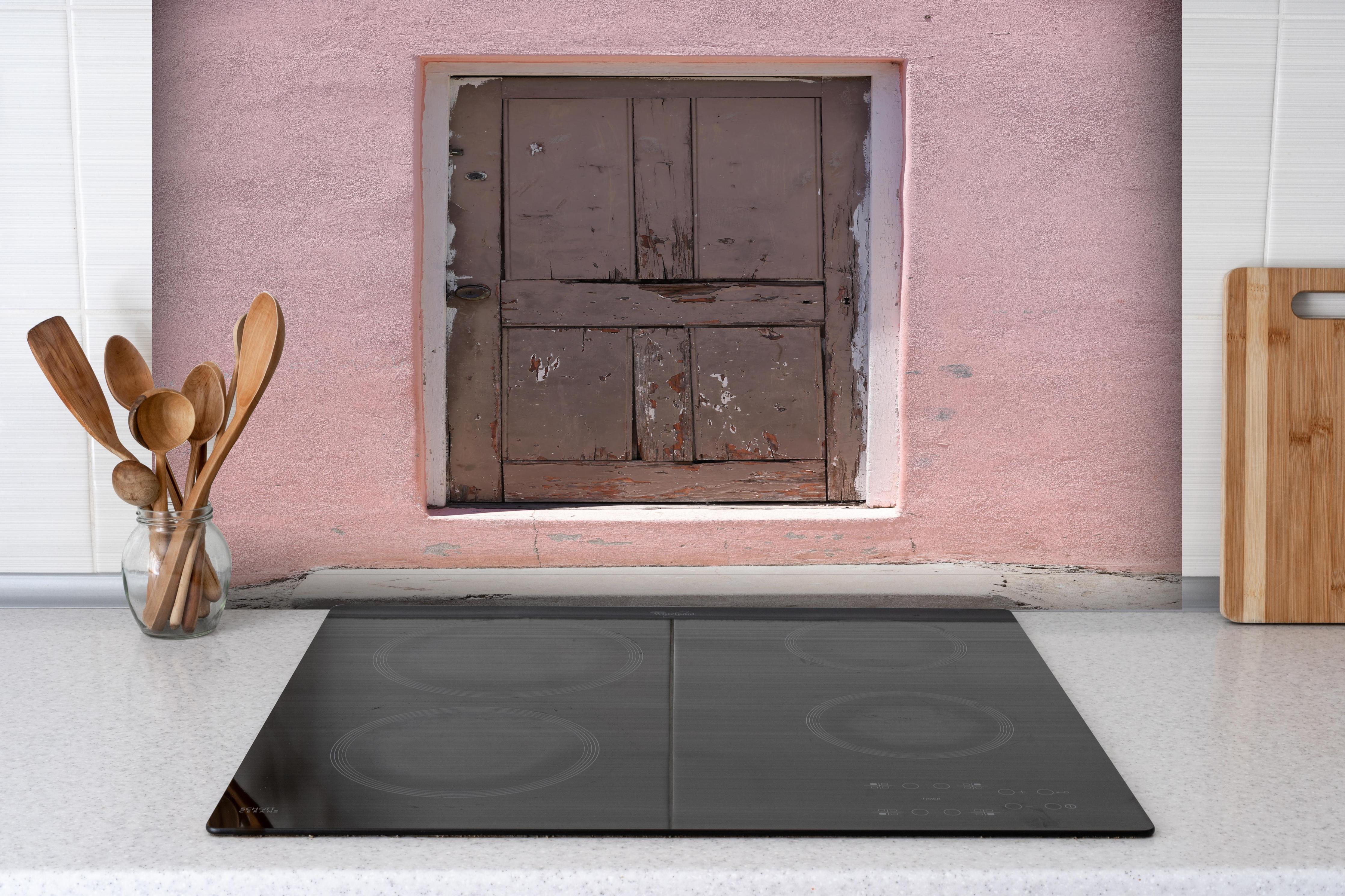 Spritzschutz - Alte Tür mit abblätternder Farbe an Rosa Wand hinter einem Cerankochfeld zwischen Holz-Kochutensilien
