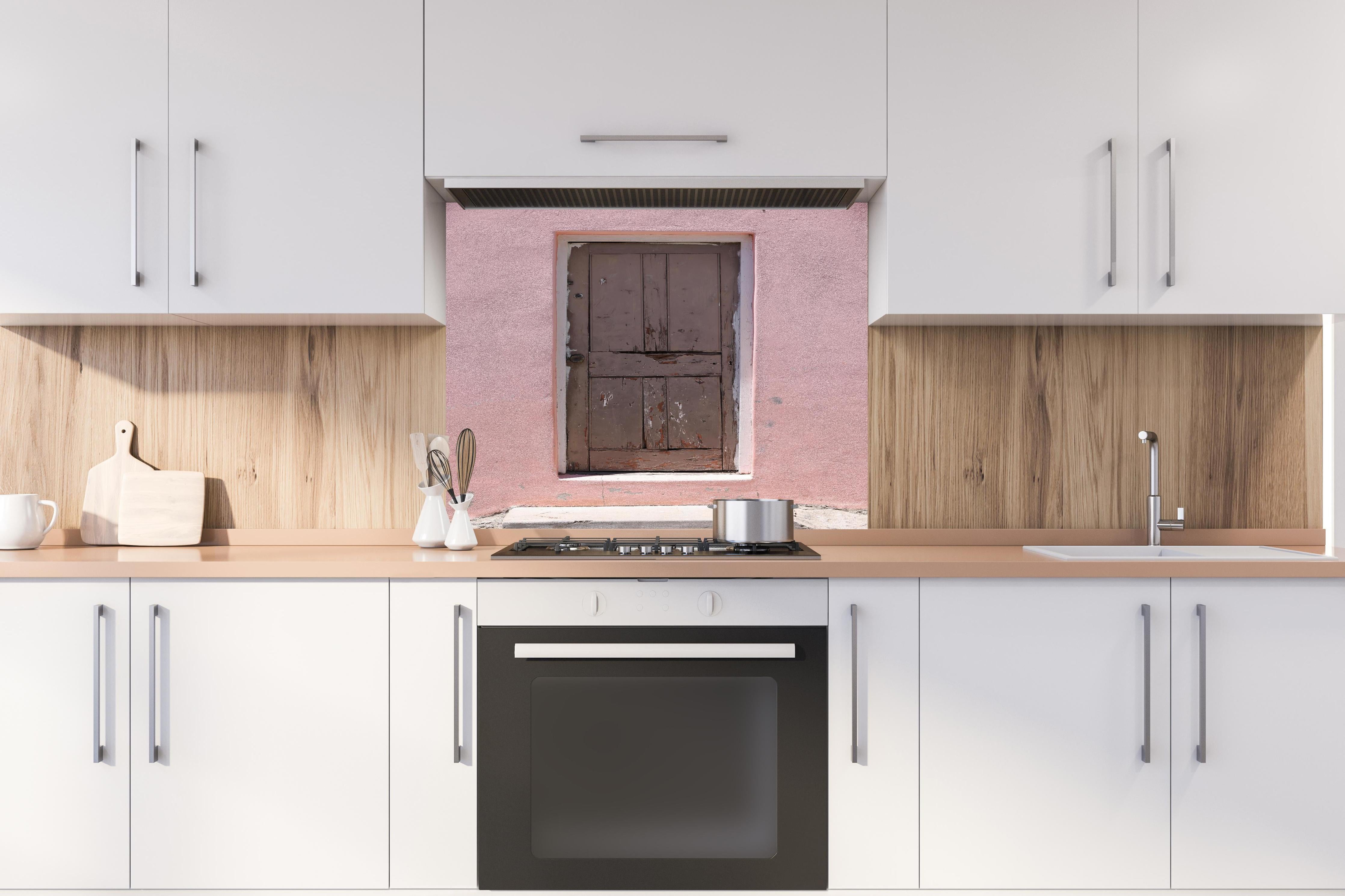 Spritzschutz - Alte Tür mit abblätternder Farbe an Rosa Wand hinter einem Cerankochfeld zwischen Holz-Kochutensilien