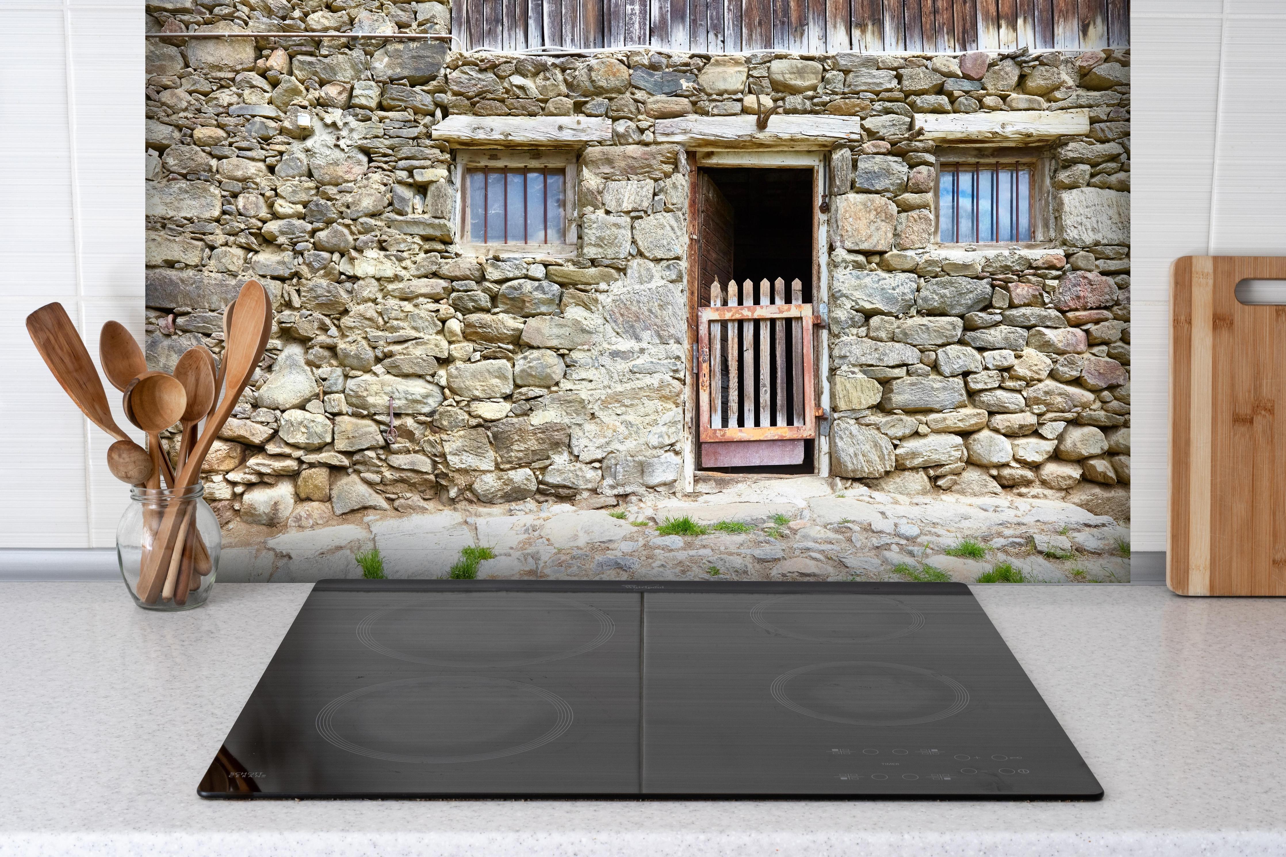 Spritzschutz - Alter Tierstall in Südtirol hinter einem Cerankochfeld zwischen Holz-Kochutensilien