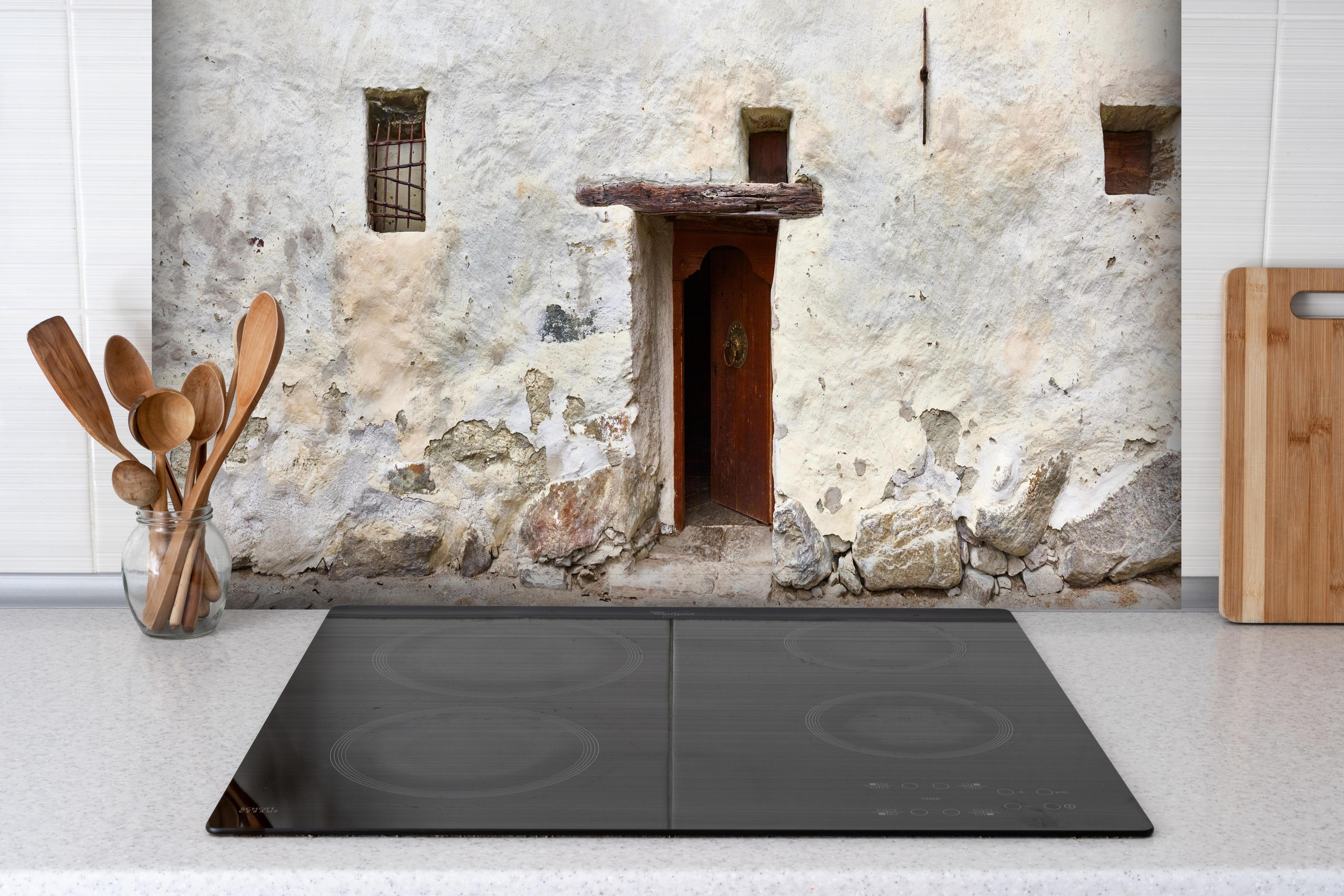 Spritzschutz - Alter Türeingang in Südtirol hinter einem Cerankochfeld zwischen Holz-Kochutensilien