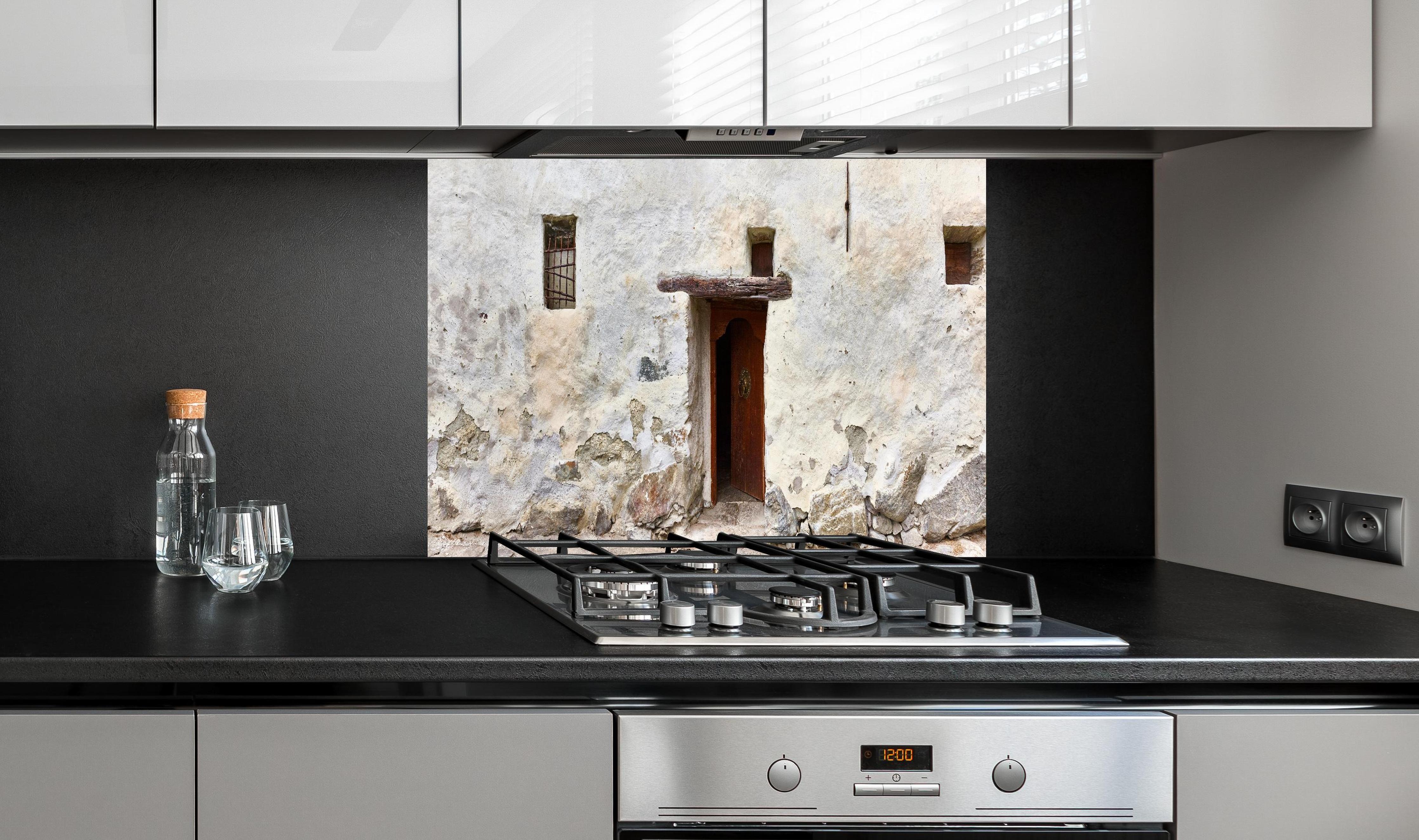 Spritzschutz - Alter Türeingang in Südtirol hinter einem Cerankochfeld zwischen Holz-Kochutensilien