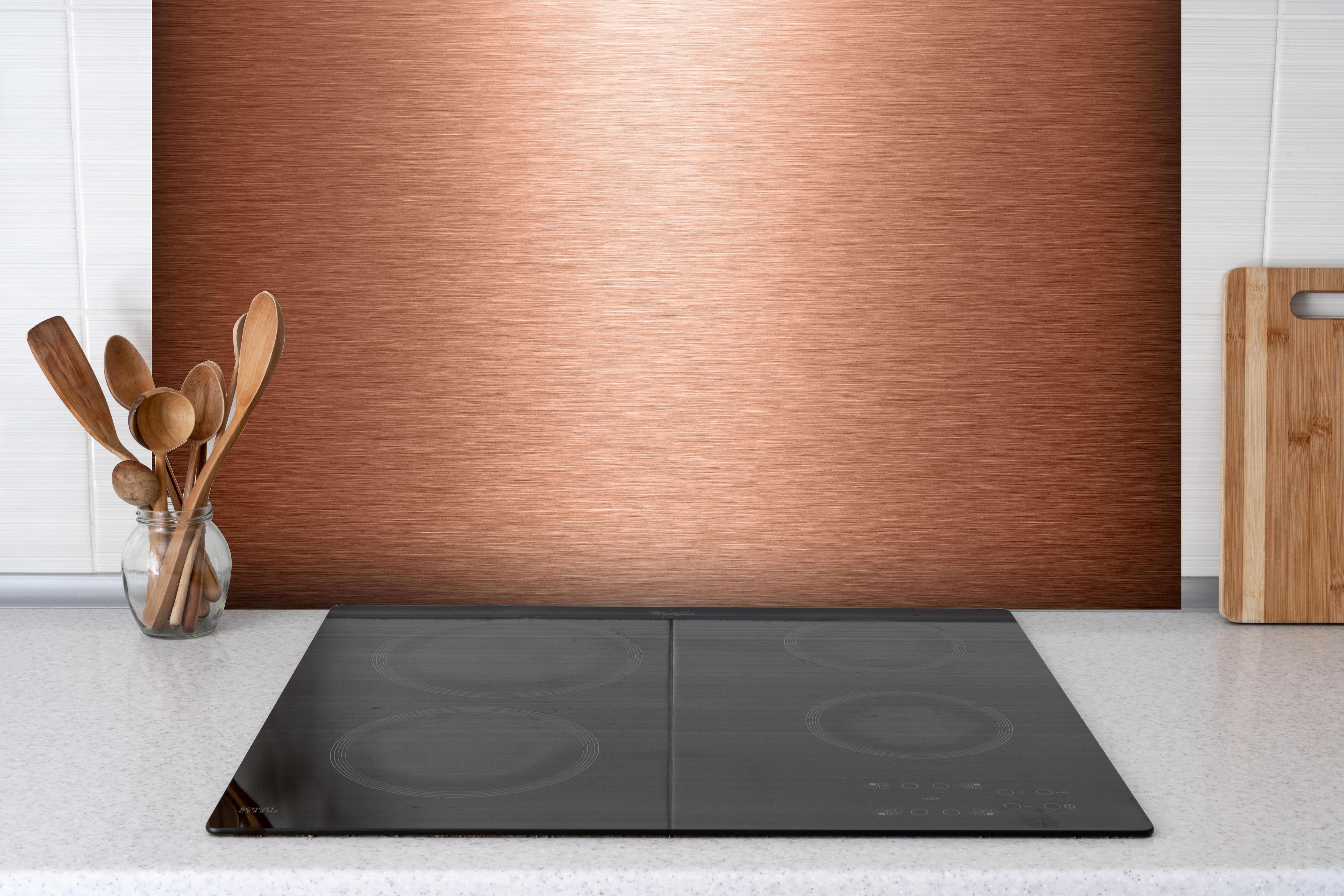 Spritzschutz - Alu gebürstet kupferfarbig hinter einem Cerankochfeld zwischen Holz-Kochutensilien