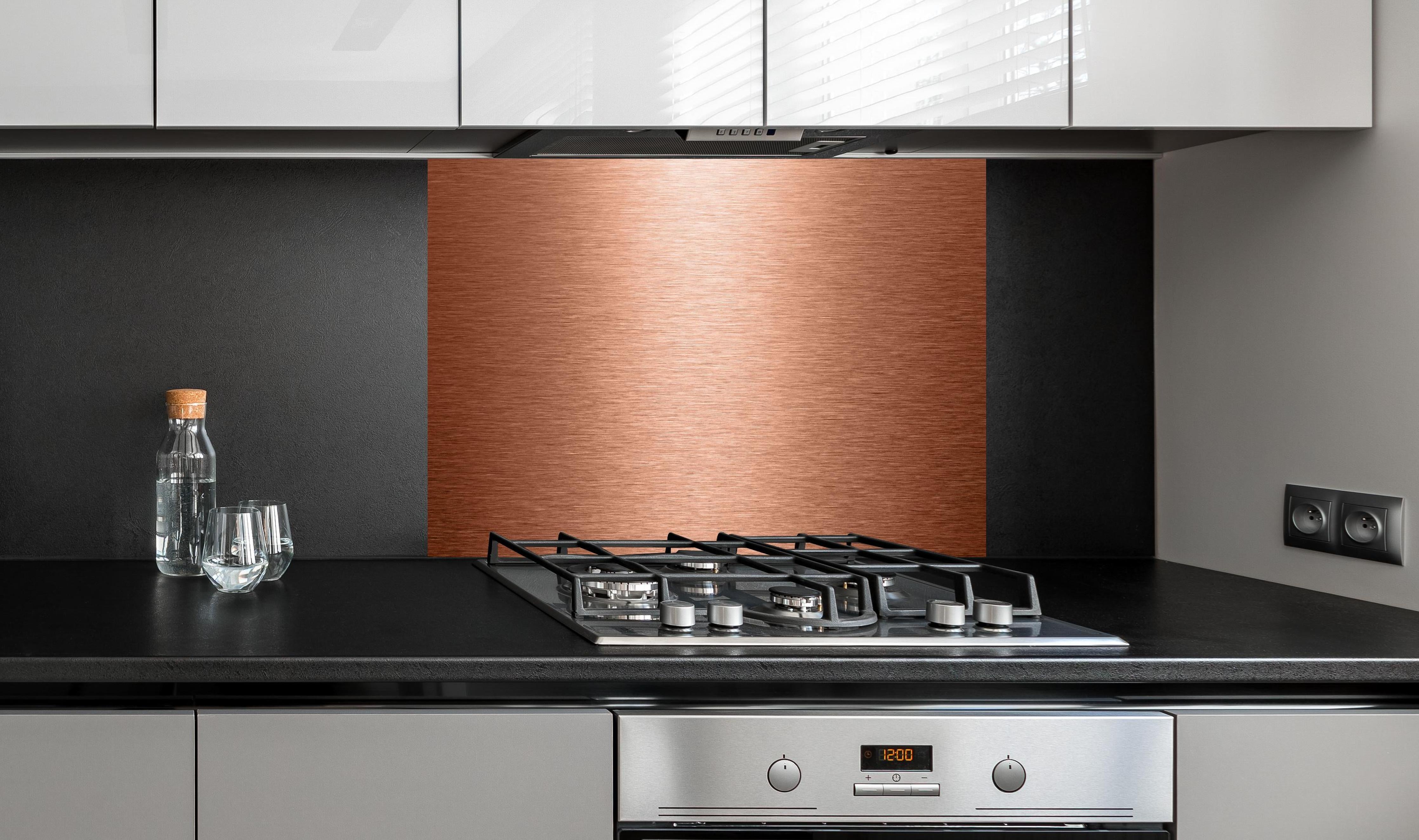 Spritzschutz - Alu gebürstet kupferfarbig hinter einem Cerankochfeld zwischen Holz-Kochutensilien