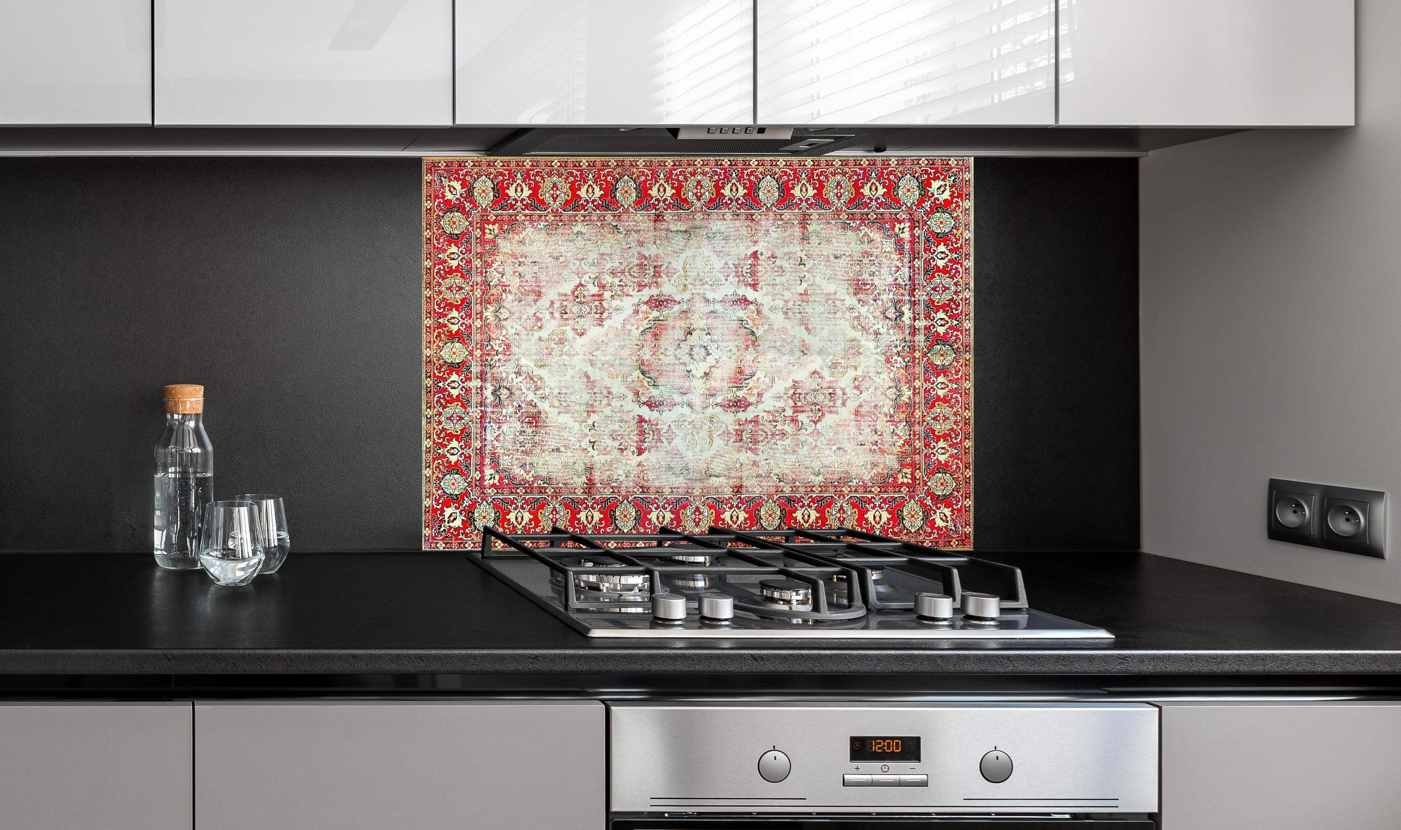 Spritzschutz - Antiker Rot-Beige-Wollteppich mit Muster hinter einem Cerankochfeld zwischen Holz-Kochutensilien