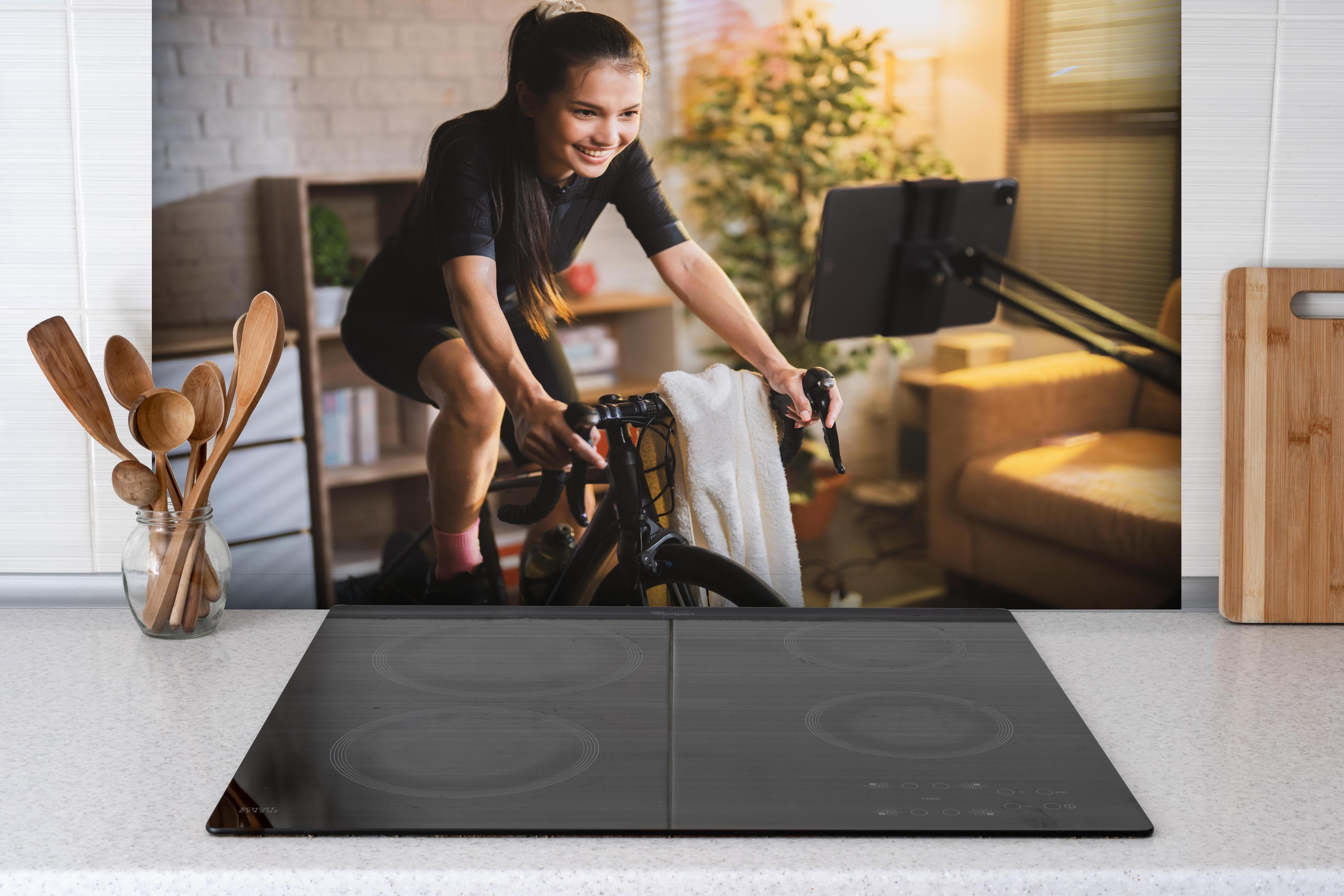 Spritzschutz - Asiatische Radfahrerin hinter einem Cerankochfeld zwischen Holz-Kochutensilien