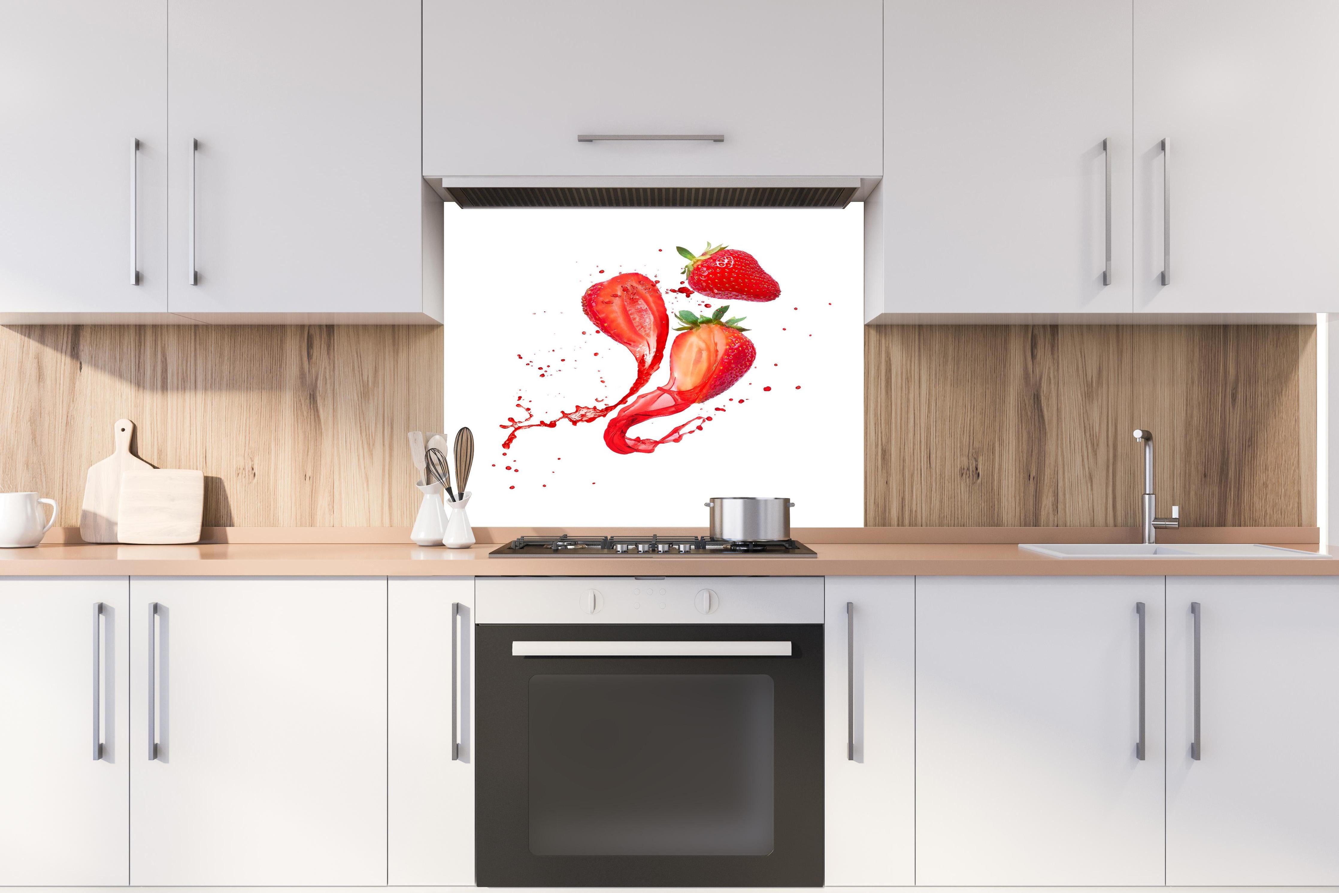 Spritzschutz - Aufgeschnittene Erdbeeren auf weißem Hintergrund hinter einem Cerankochfeld zwischen Holz-Kochutensilien
