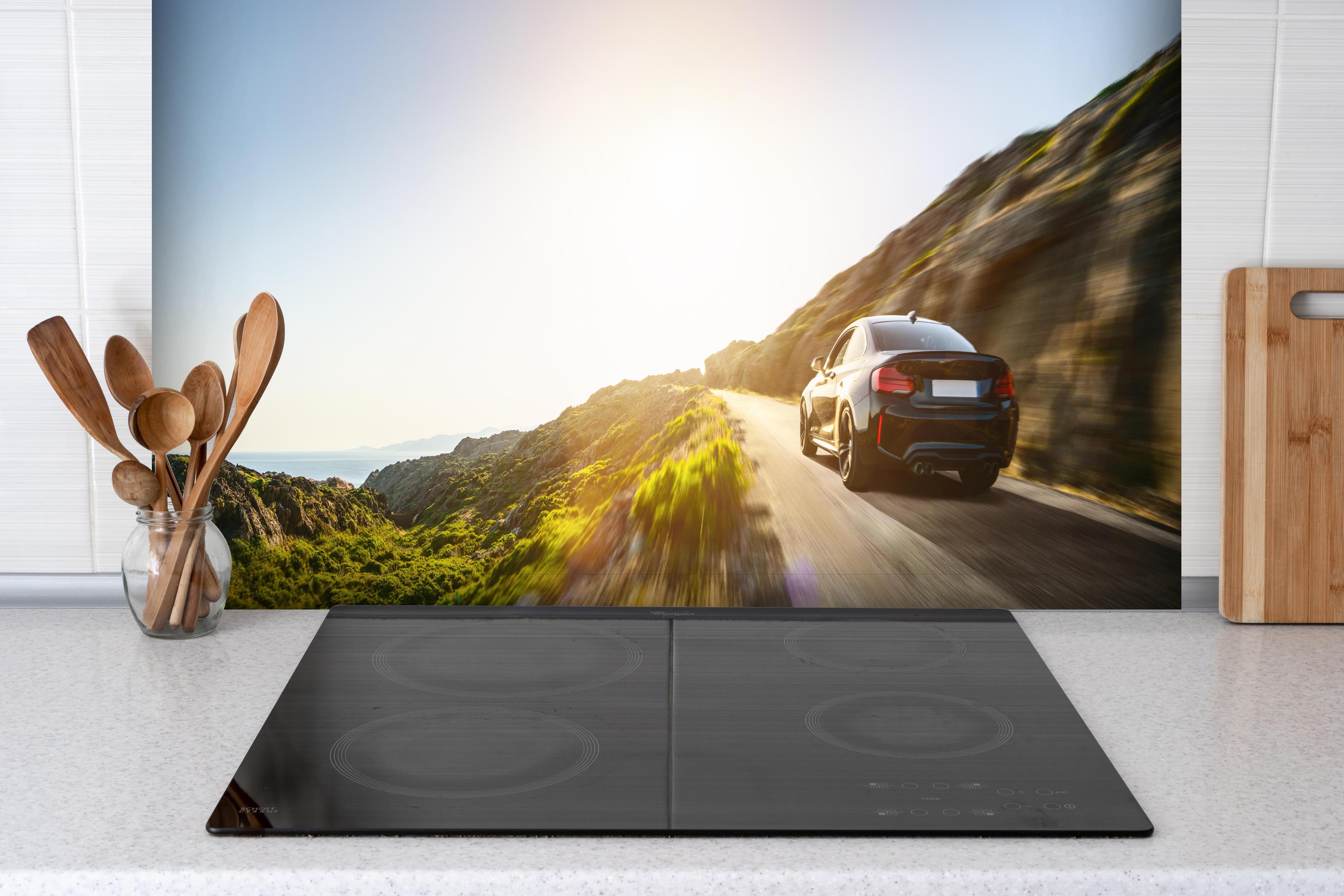 Spritzschutz - Auto fährt über eine Straße auf Bergen hinter einem Cerankochfeld zwischen Holz-Kochutensilien