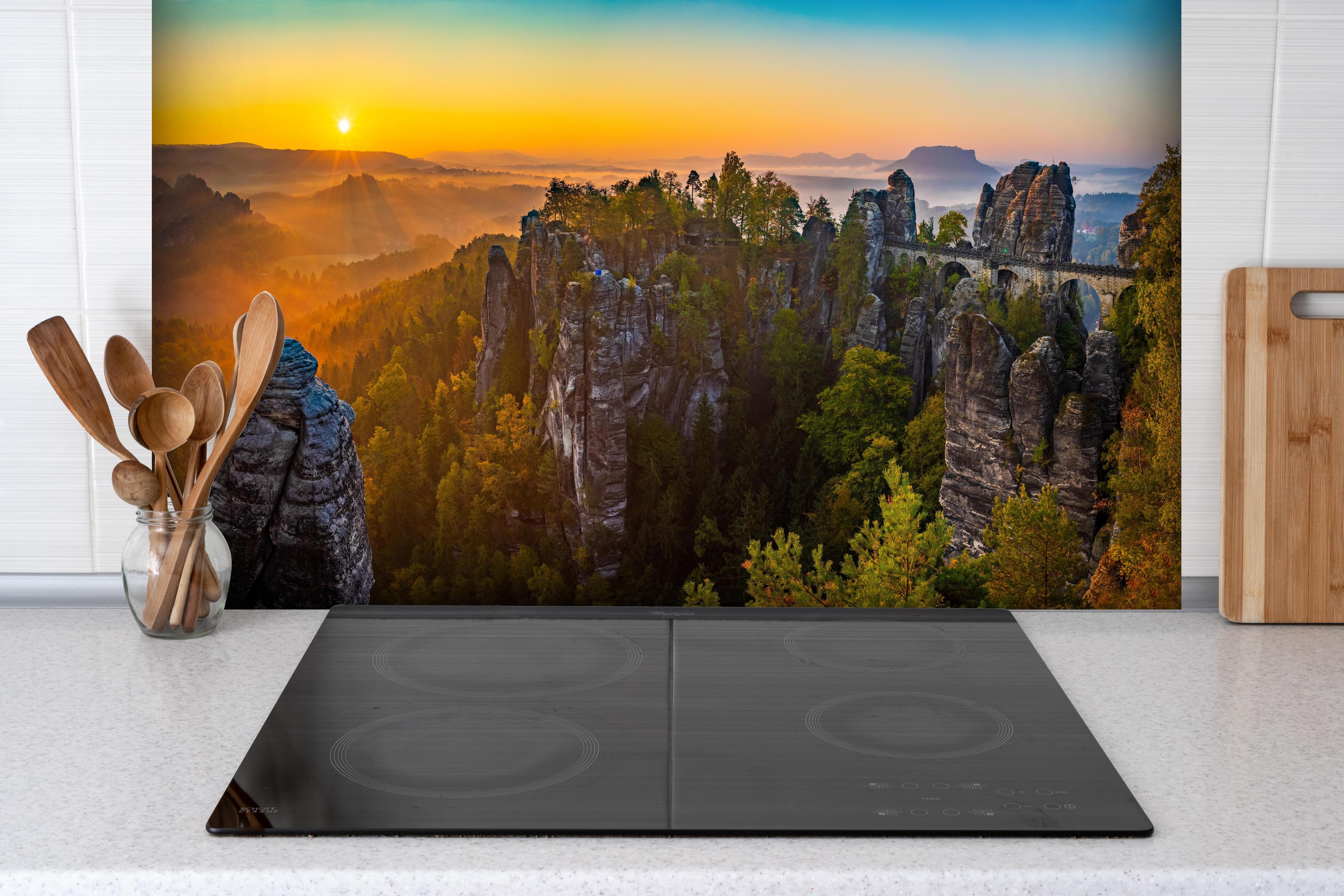 Spritzschutz - Basteibrücke Sonnenaufgang Felsformationen hinter einem Cerankochfeld zwischen Holz-Kochutensilien