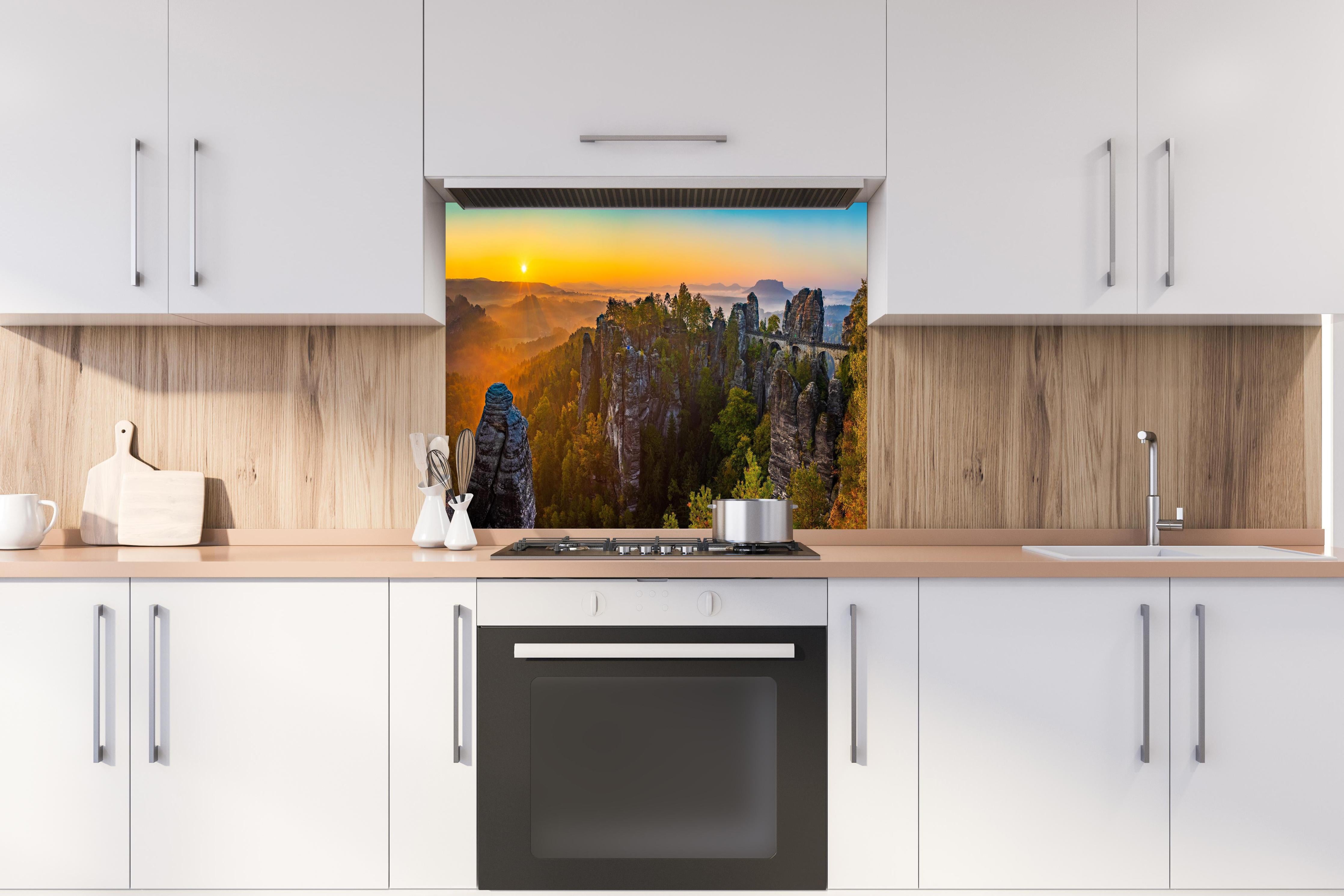 Spritzschutz - Basteibrücke Sonnenaufgang Felsformationen hinter einem Cerankochfeld zwischen Holz-Kochutensilien