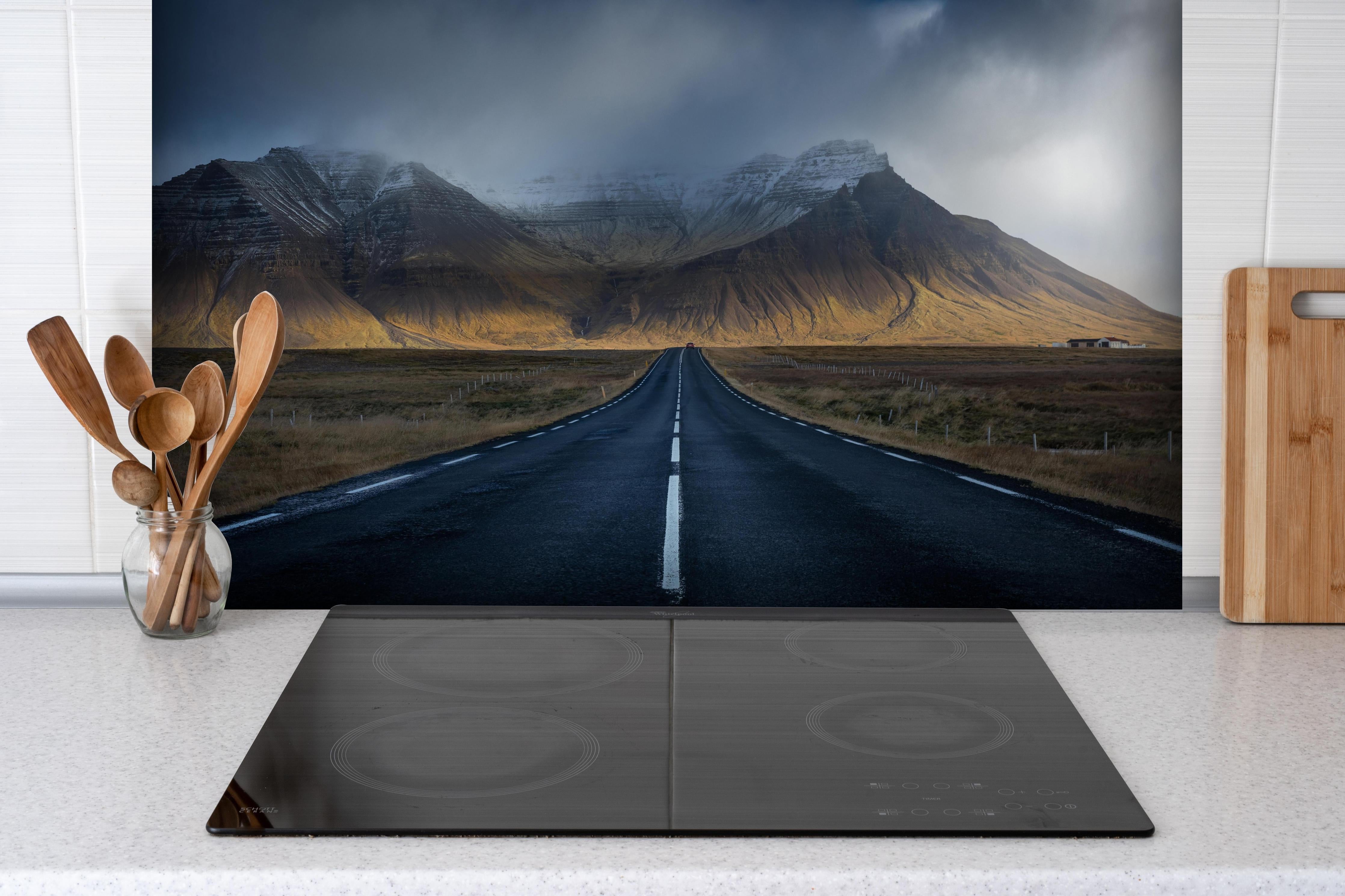 Spritzschutz - Beeindruckende Straße durch isländische Bergwelt hinter einem Cerankochfeld zwischen Holz-Kochutensilien