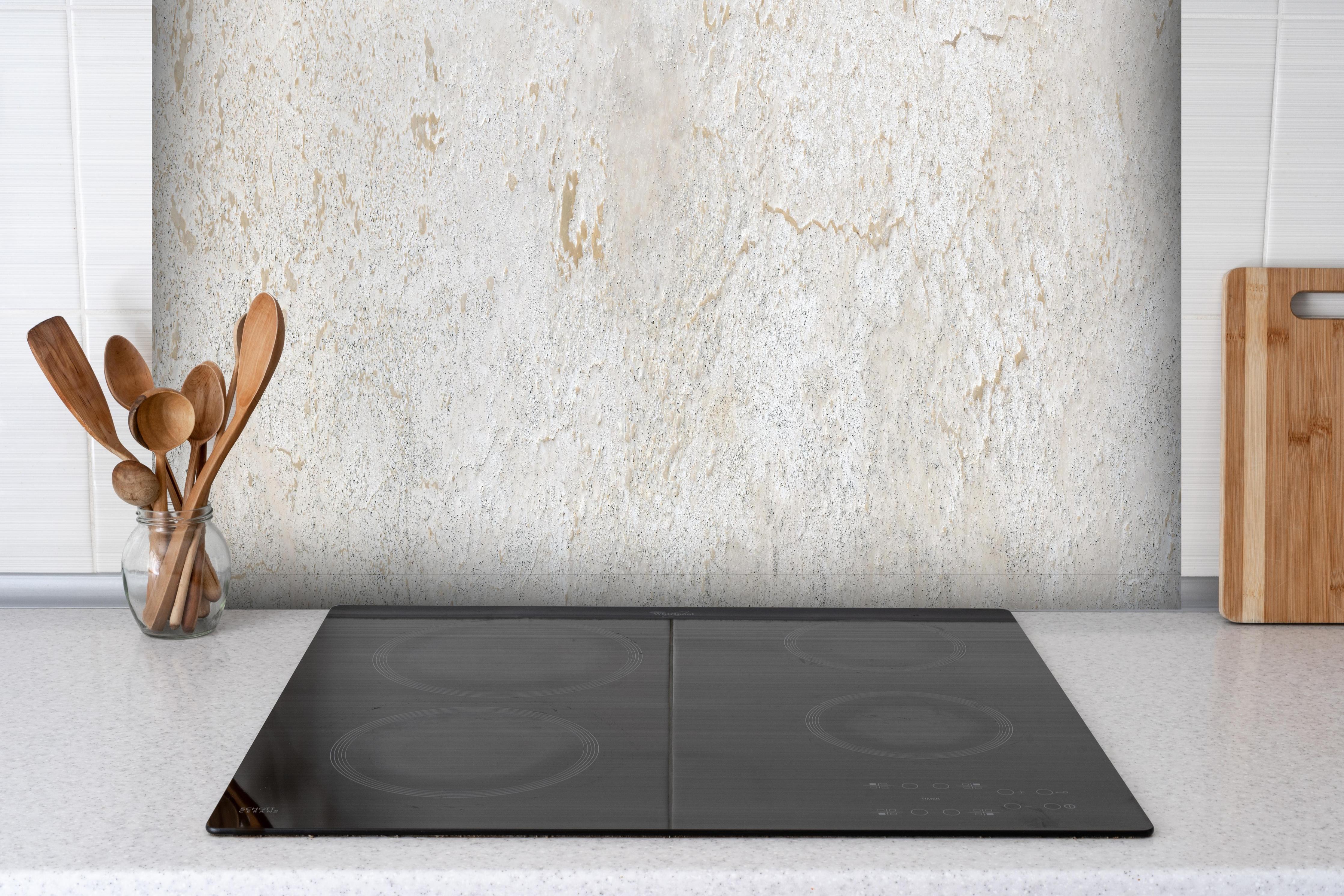 Spritzschutz - Beiger Kalkstein hinter einem Cerankochfeld zwischen Holz-Kochutensilien