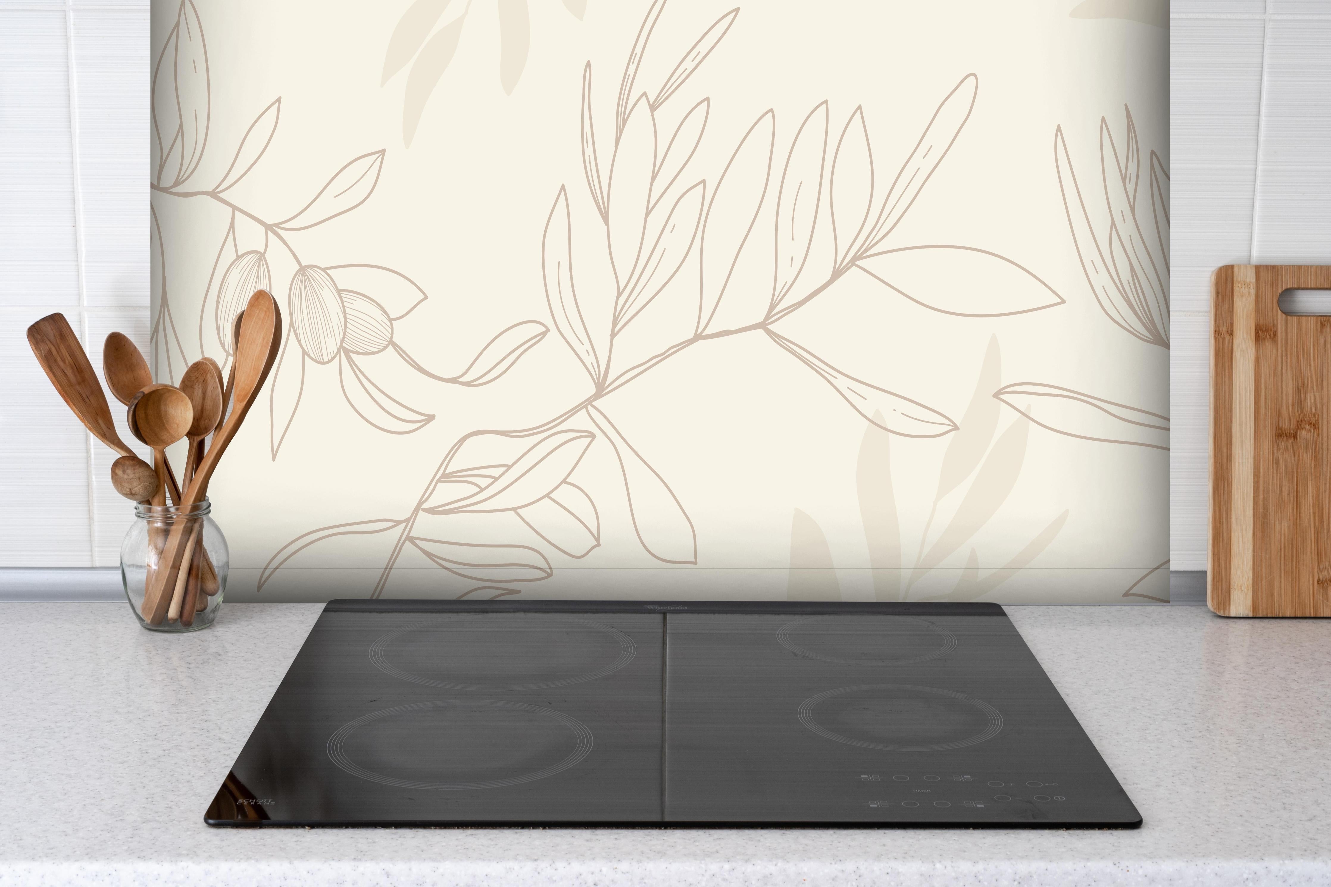 Spritzschutz - Beiger Olivenzweig hinter einem Cerankochfeld zwischen Holz-Kochutensilien