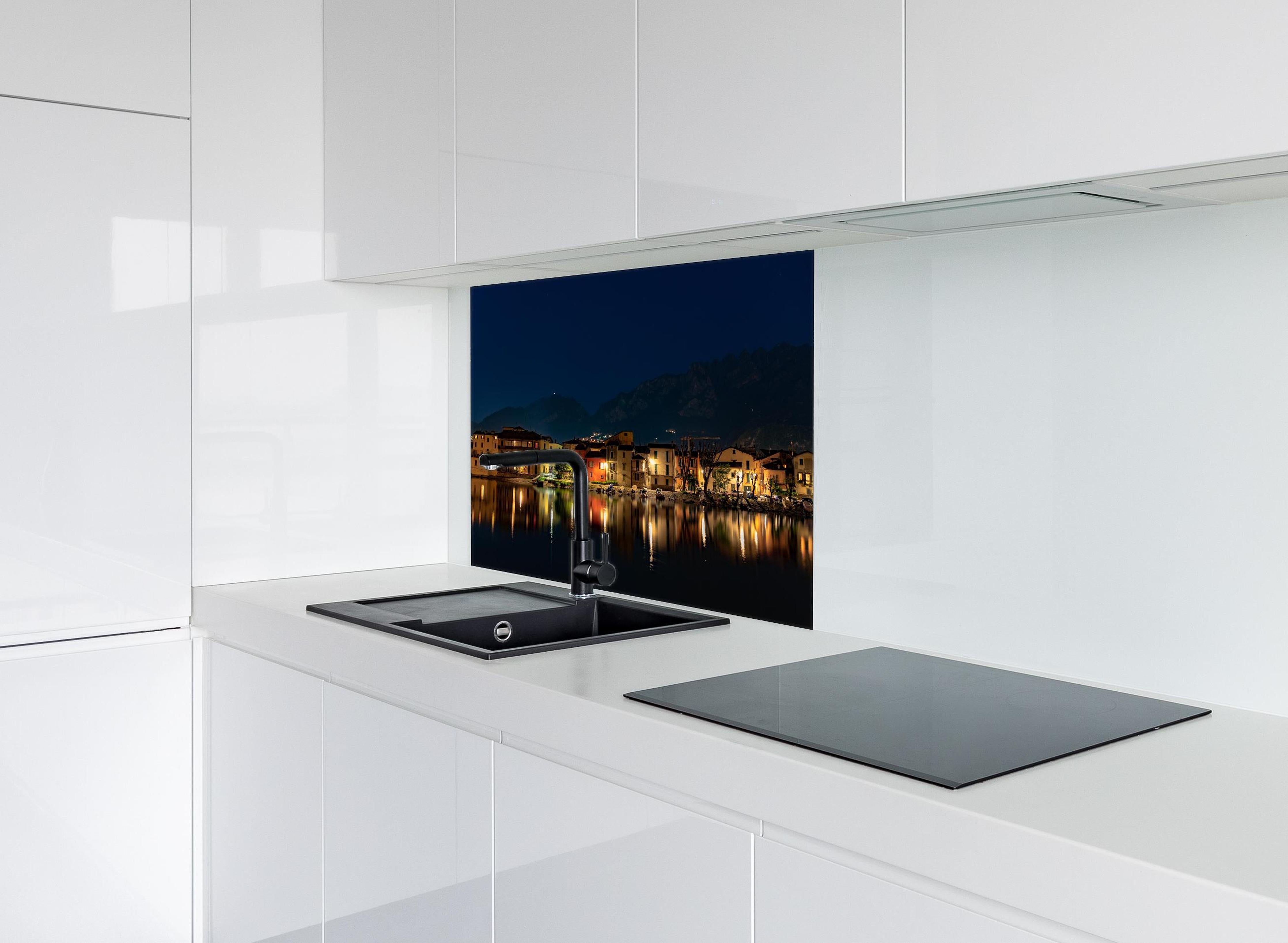 Spritzschutz - Beleuchtete Seelandschaft bei Nacht hinter einem Cerankochfeld zwischen Holz-Kochutensilien