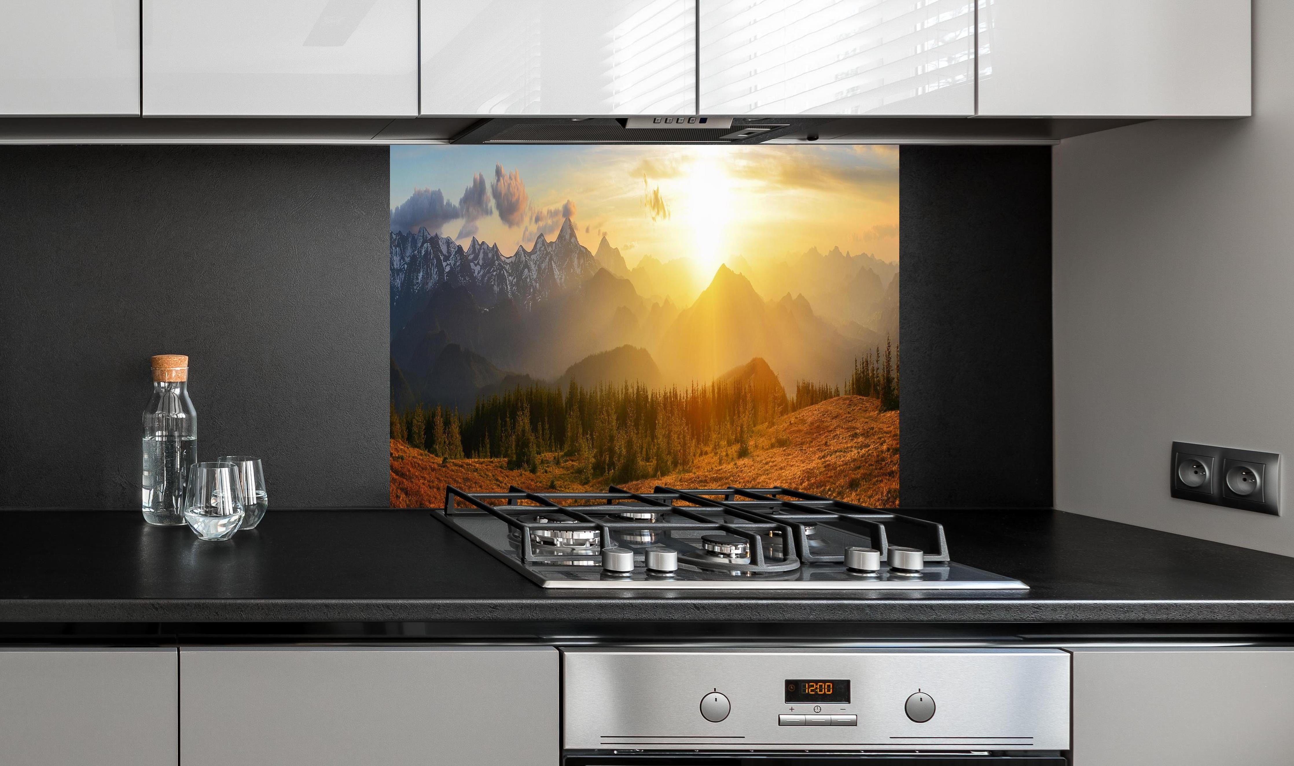 Spritzschutz - Berge im Sonnenuntergang hinter einem Cerankochfeld zwischen Holz-Kochutensilien