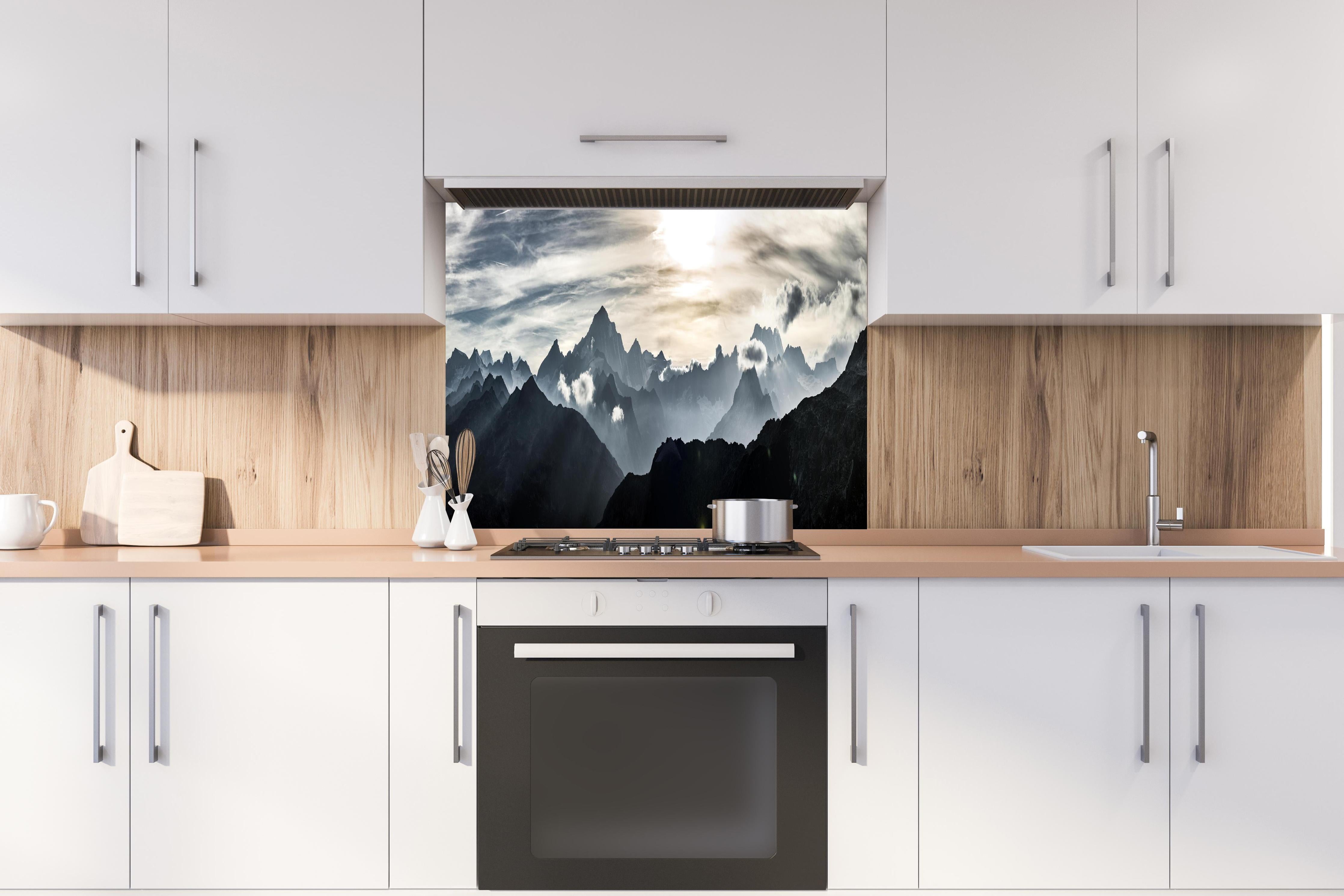 Spritzschutz - Bergpanorama mit Sonnenuntergangslicht hinter einem Cerankochfeld zwischen Holz-Kochutensilien