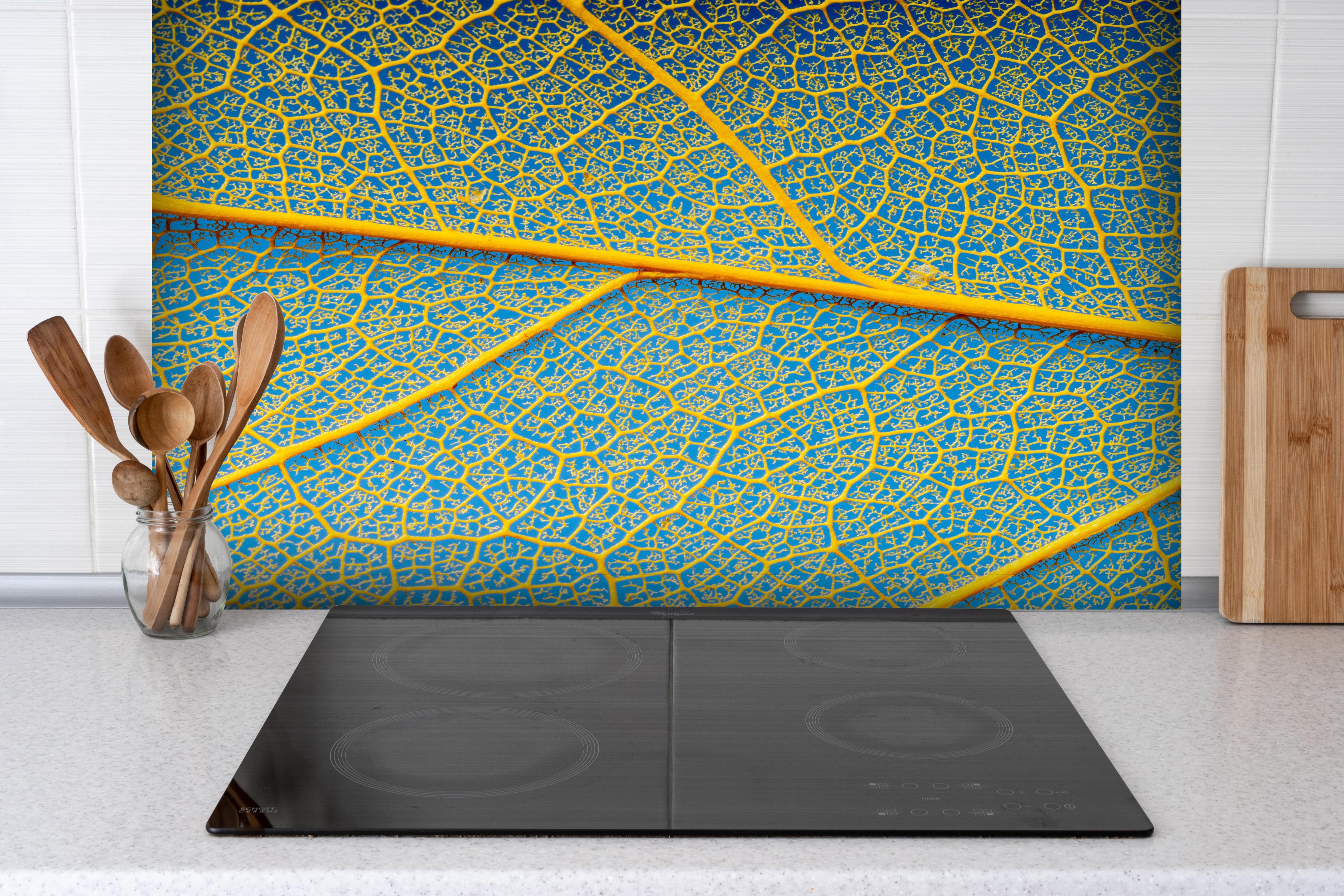 Spritzschutz - Blattstruktur in Makroaufnahme Gelb-Blau hinter einem Cerankochfeld zwischen Holz-Kochutensilien