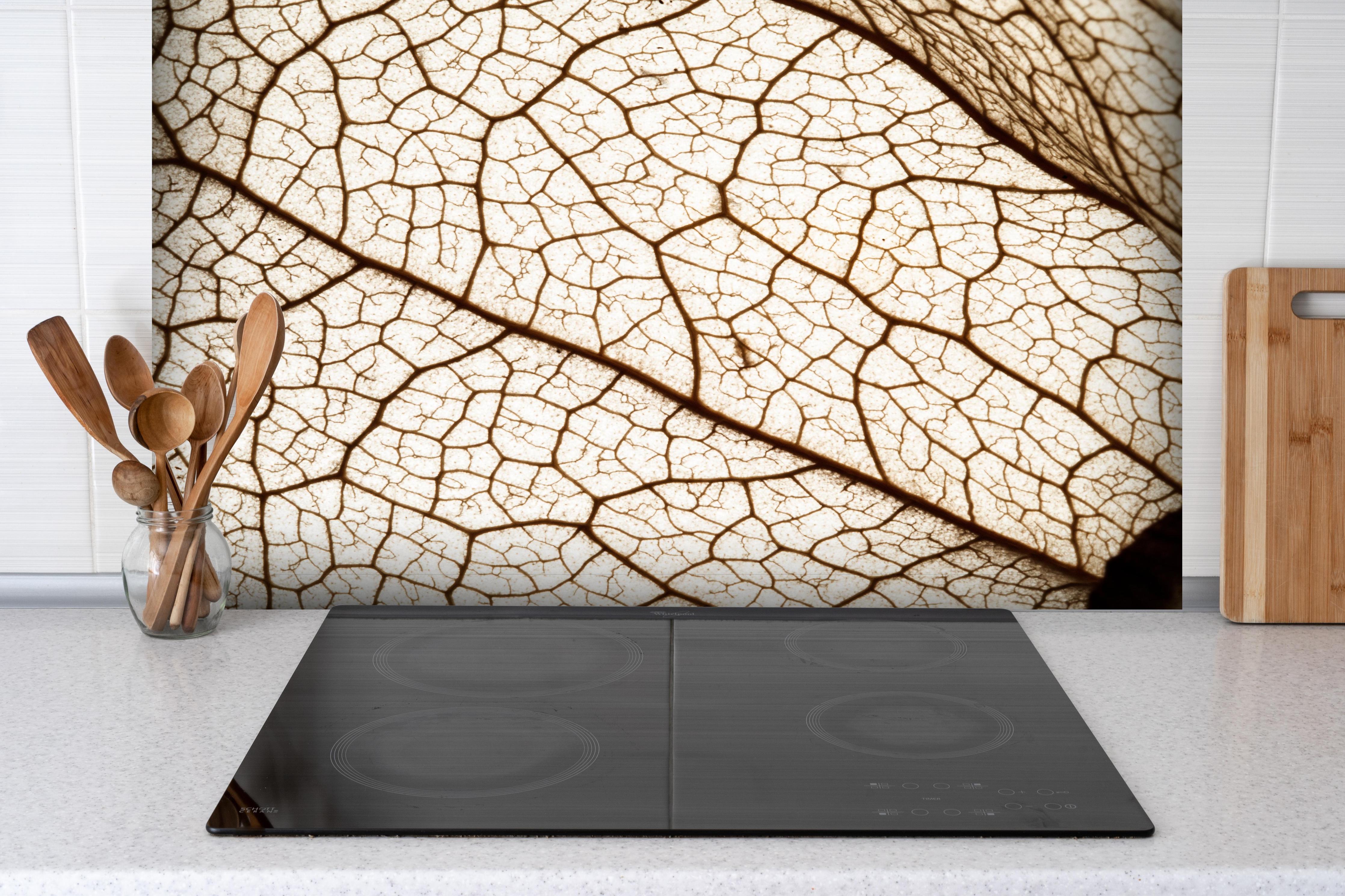 Spritzschutz - Blatttextur im Detail hinter einem Cerankochfeld zwischen Holz-Kochutensilien
