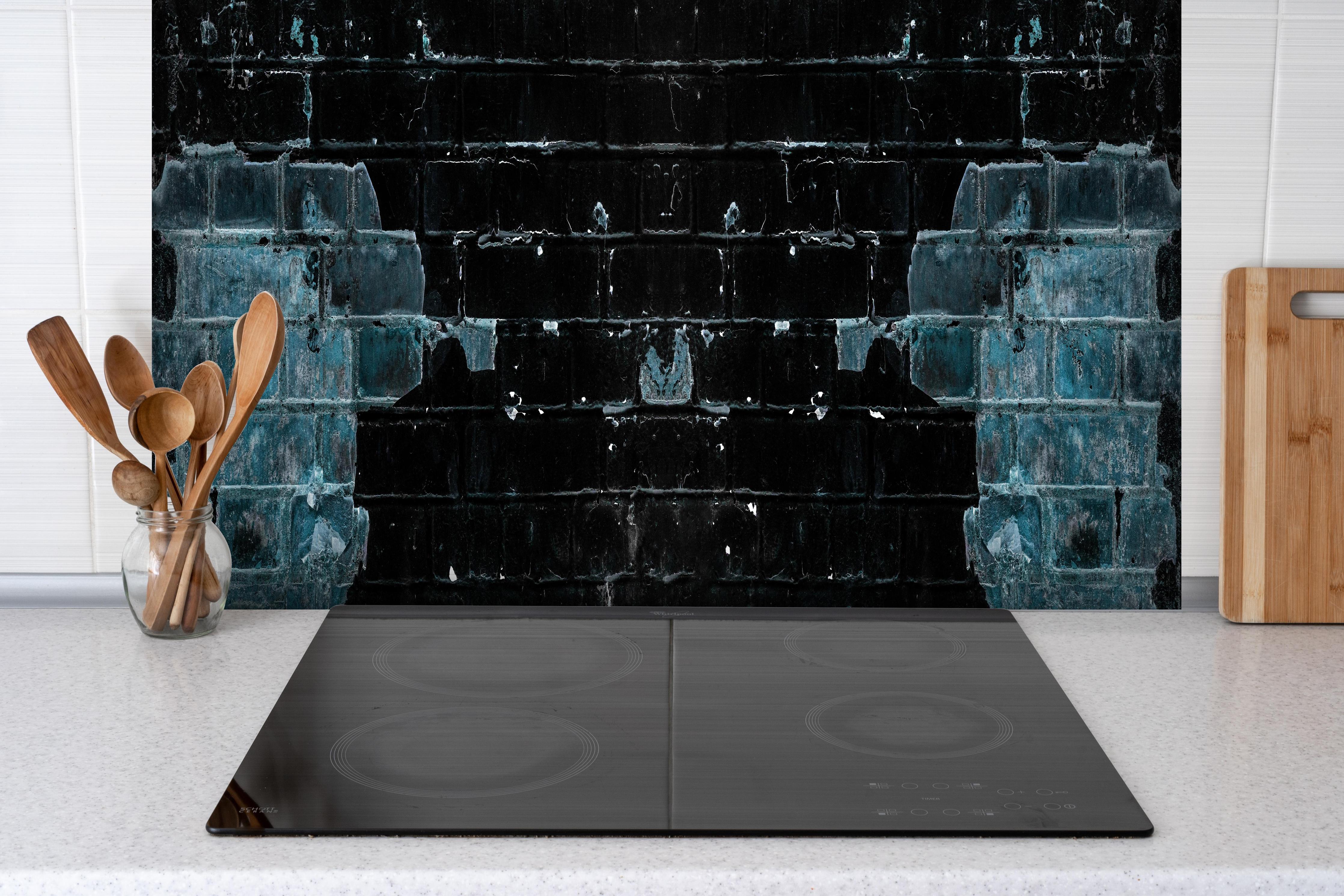 Spritzschutz - Blau schwarz beschädigte Ziegelwand hinter einem Cerankochfeld zwischen Holz-Kochutensilien