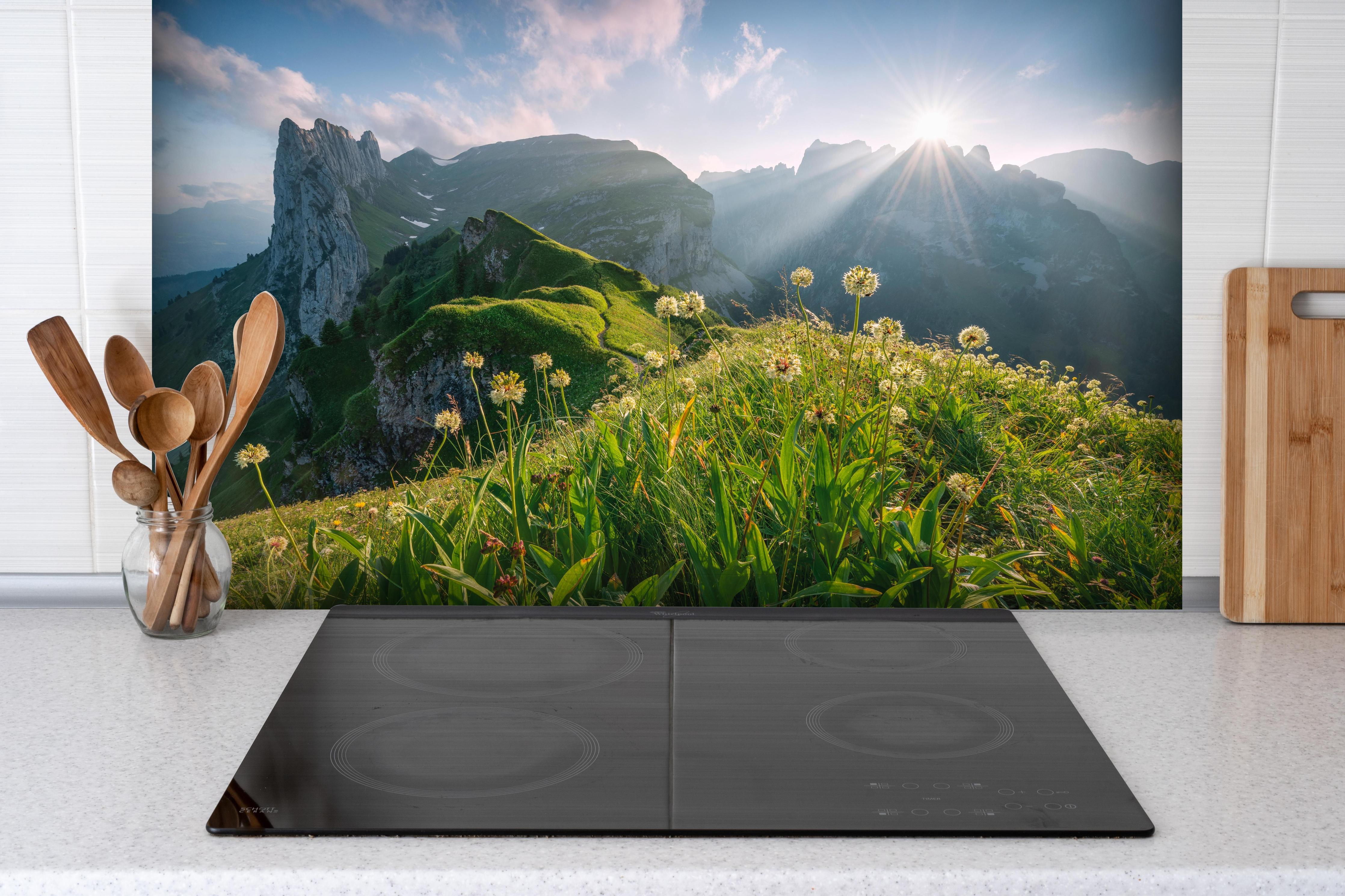 Spritzschutz - Blühende Alpenwiesen bei Sonnenaufgang hinter einem Cerankochfeld zwischen Holz-Kochutensilien