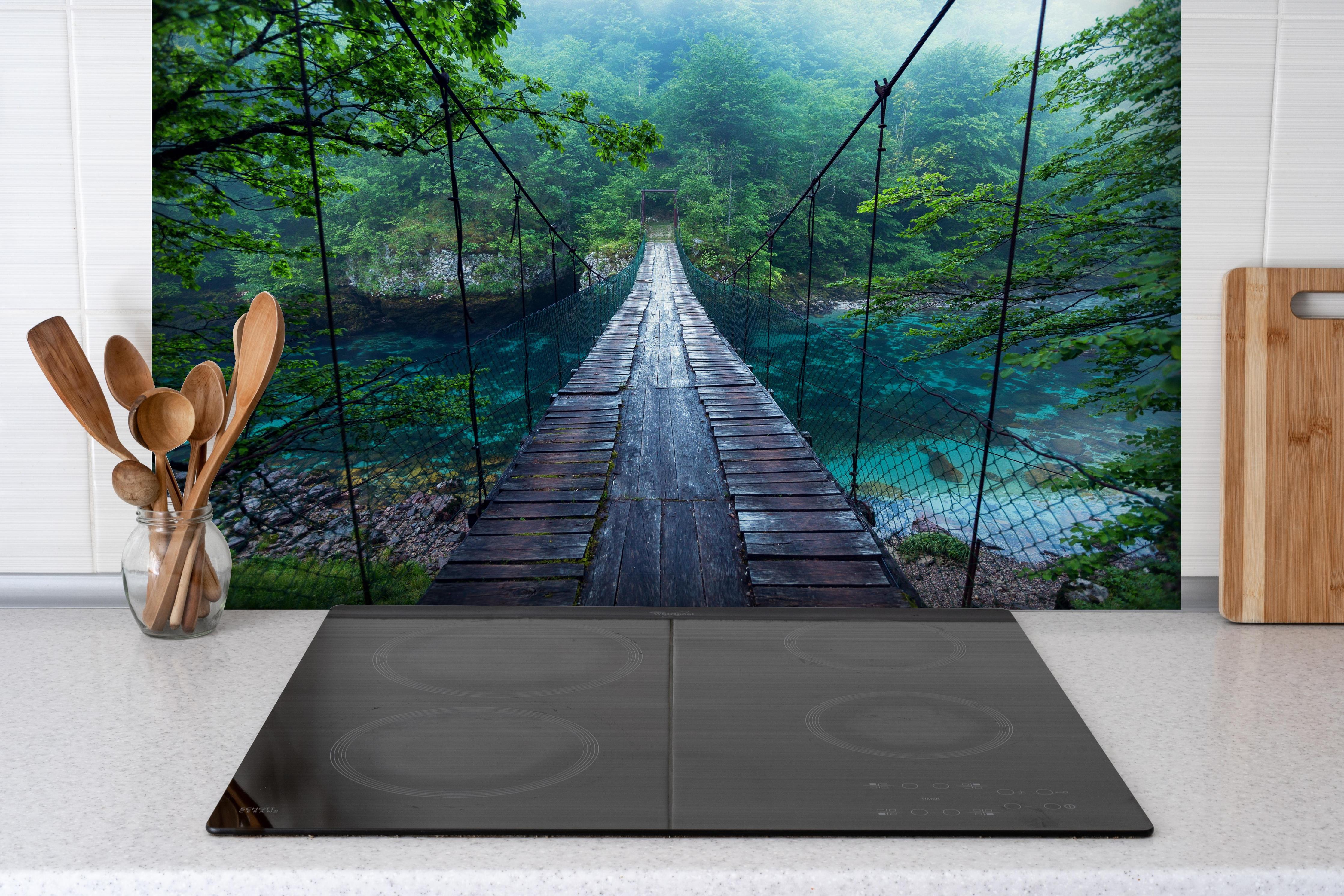 Spritzschutz - Brücke über Kristallklarem Fluss hinter einem Cerankochfeld zwischen Holz-Kochutensilien