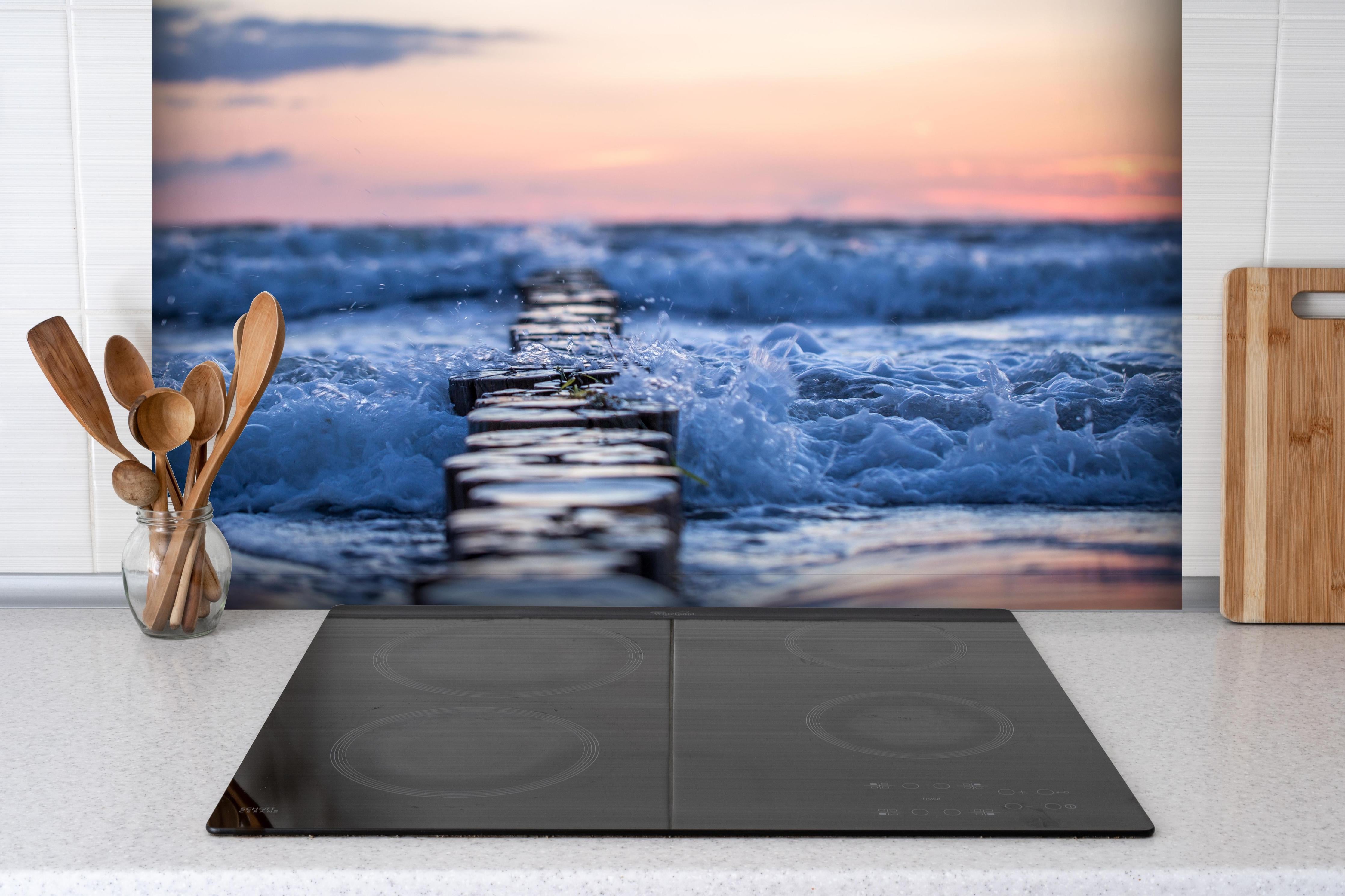 Spritzschutz - Buhnen im Meer bei Sonnenaufgang hinter einem Cerankochfeld zwischen Holz-Kochutensilien