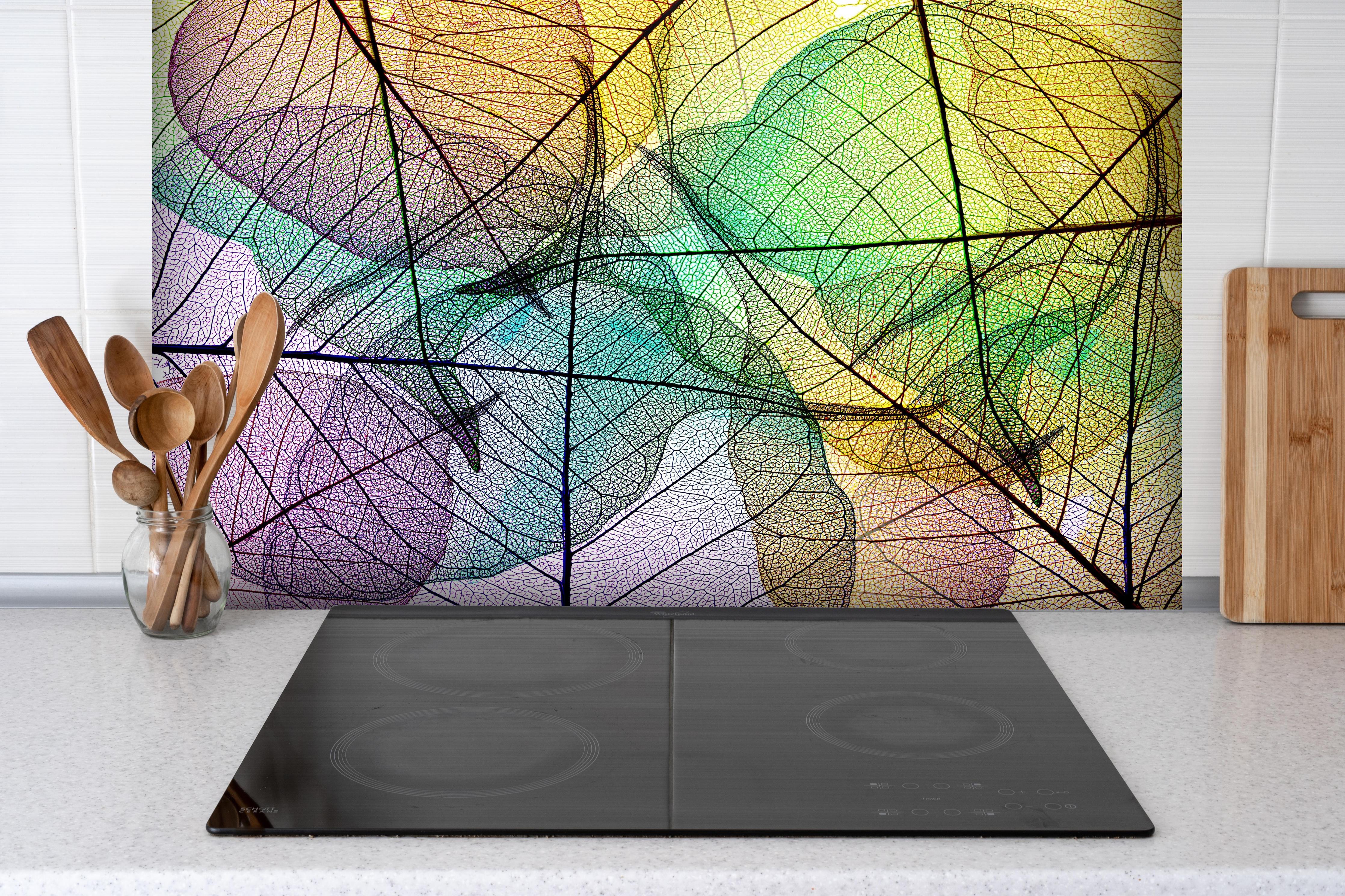 Spritzschutz - Bunte Blätter-Textur auf weißem Hintergrund hinter einem Cerankochfeld zwischen Holz-Kochutensilien