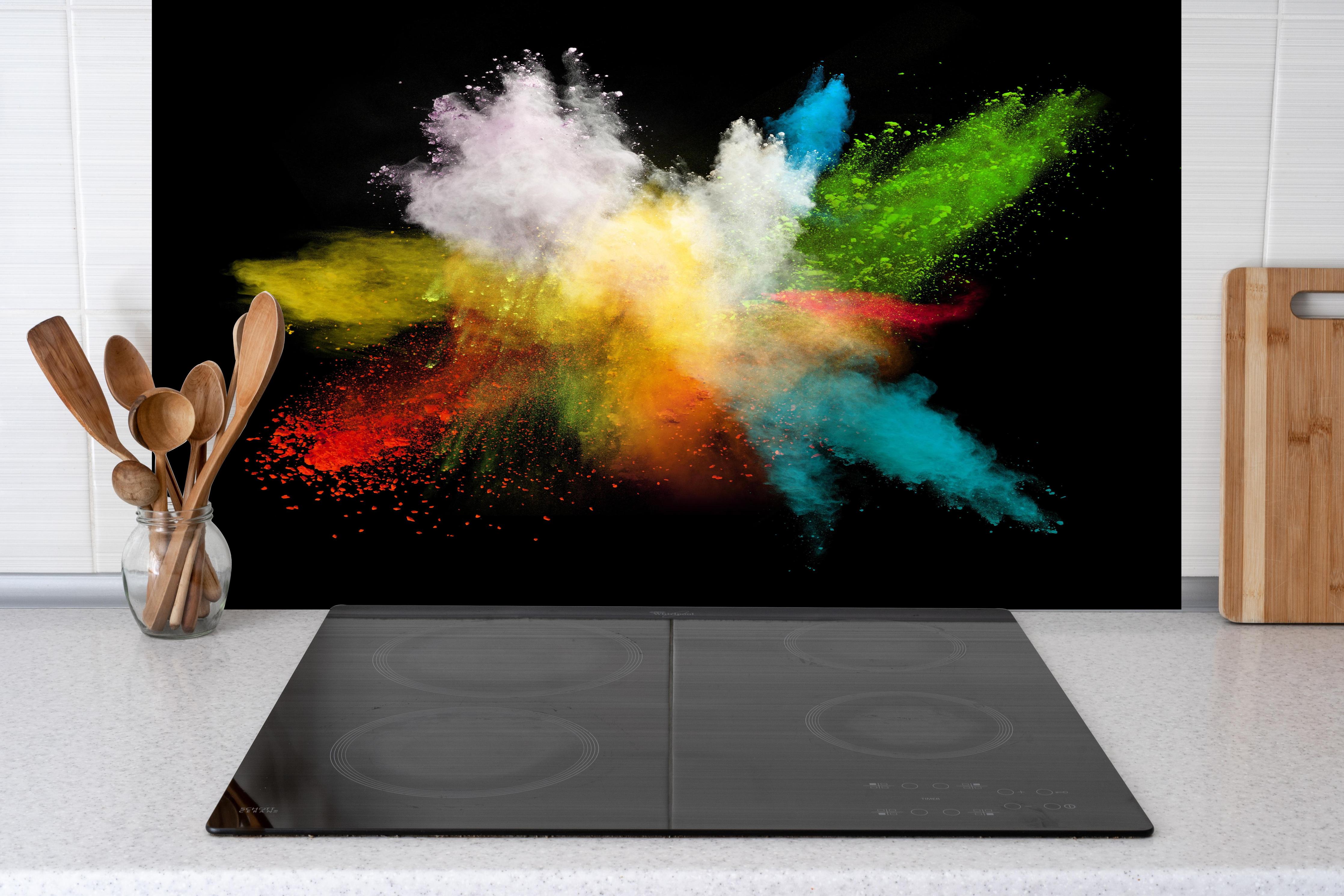 Spritzschutz - Bunte Farbexplosion auf schwarzem Hintergrund hinter einem Cerankochfeld zwischen Holz-Kochutensilien