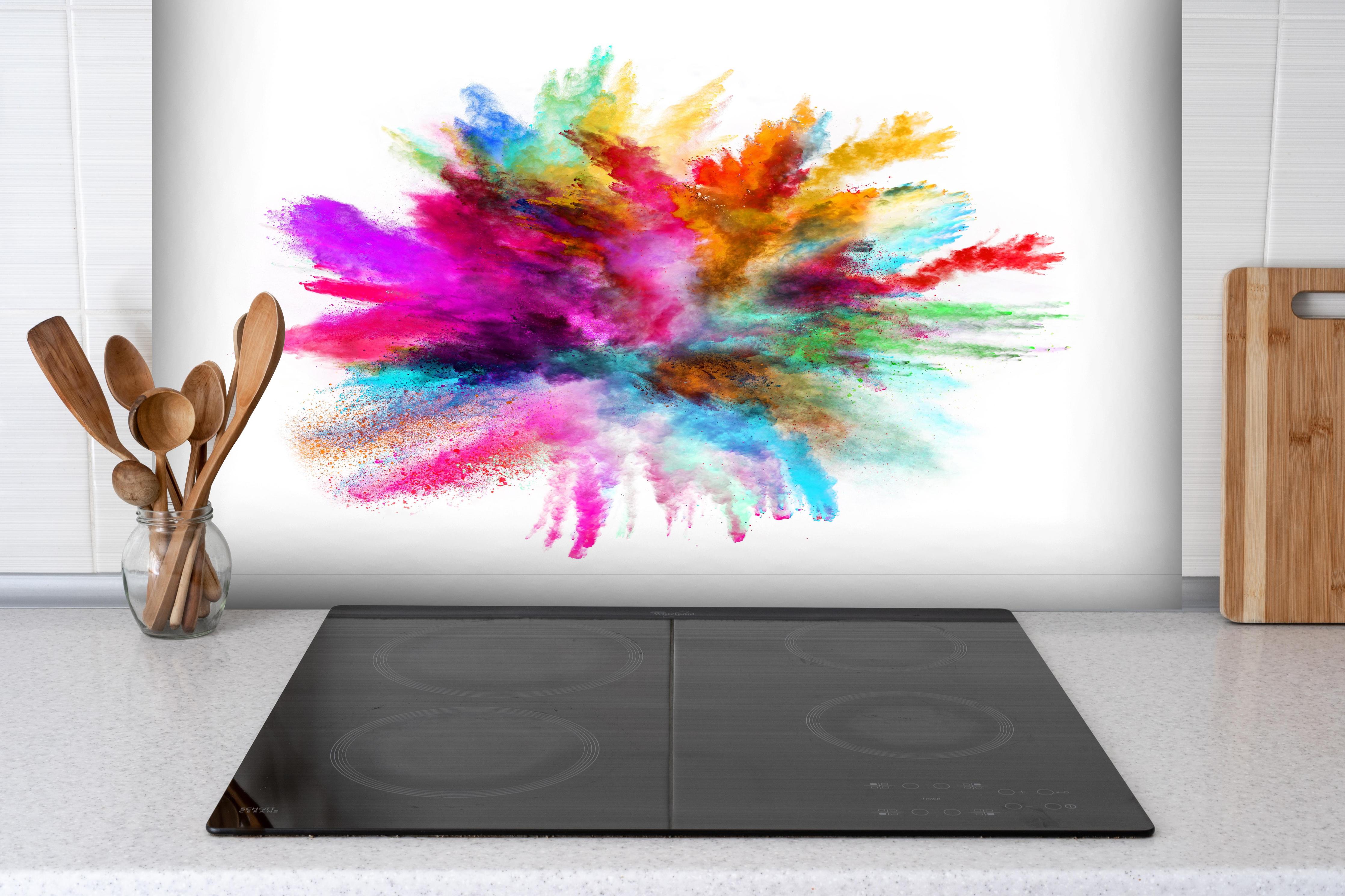 Spritzschutz - Bunte Farbexplosion auf weißen Hintergrund hinter einem Cerankochfeld zwischen Holz-Kochutensilien
