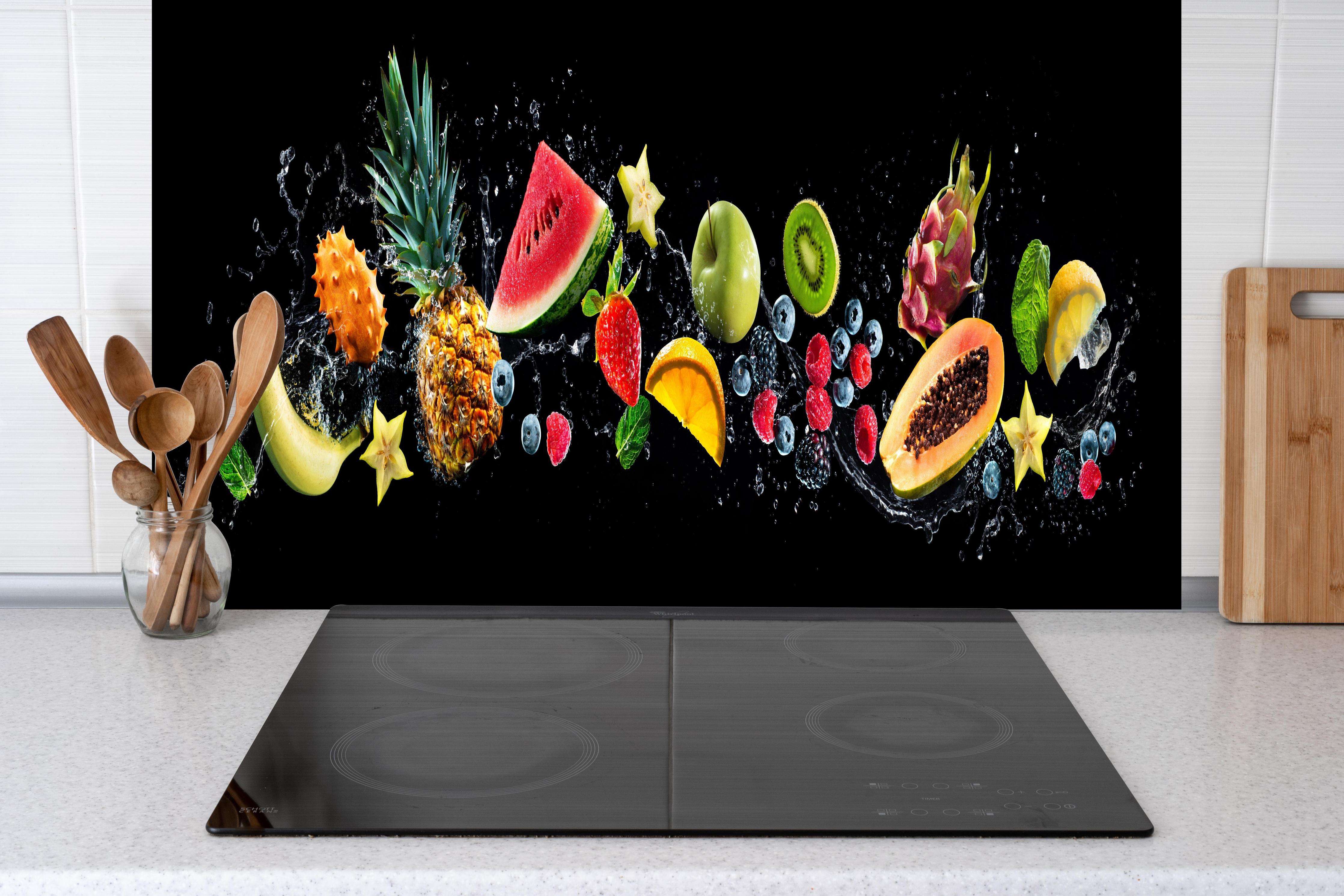 Spritzschutz - Bunte Früchte mit Wasserspritzern hinter einem Cerankochfeld zwischen Holz-Kochutensilien