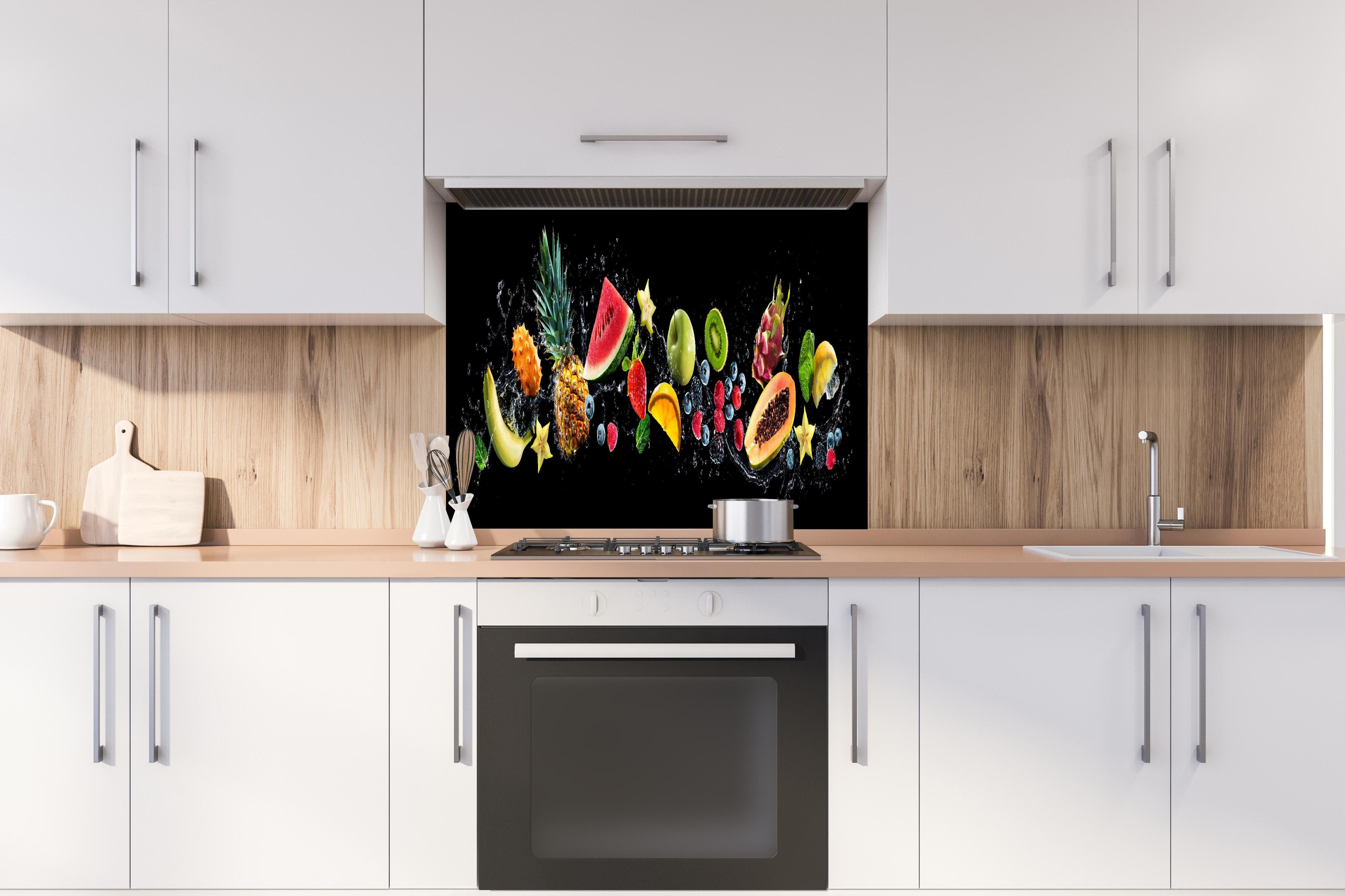 Spritzschutz - Bunte Früchte mit Wasserspritzern hinter einem Cerankochfeld zwischen Holz-Kochutensilien