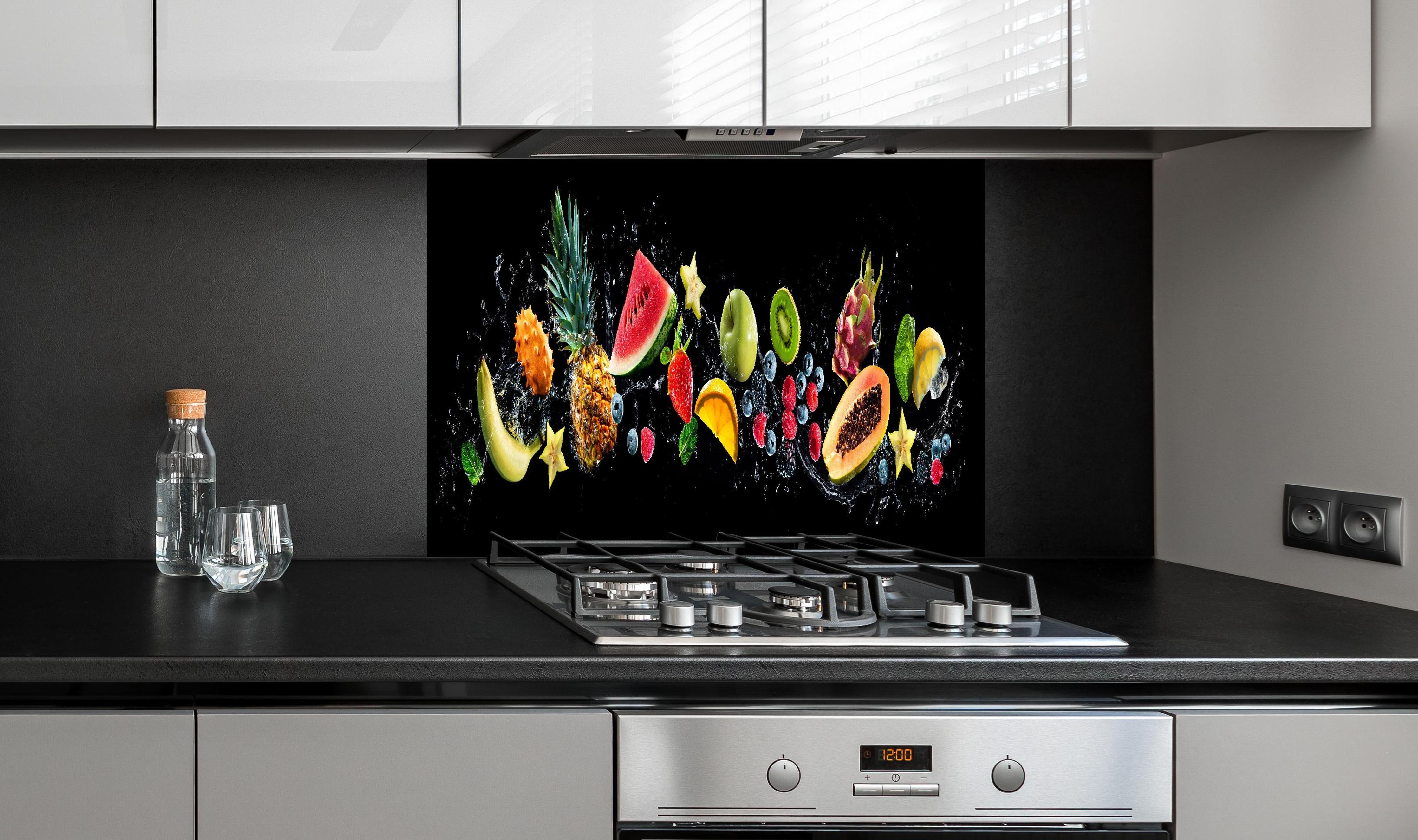 Spritzschutz - Bunte Früchte mit Wasserspritzern hinter einem Cerankochfeld zwischen Holz-Kochutensilien