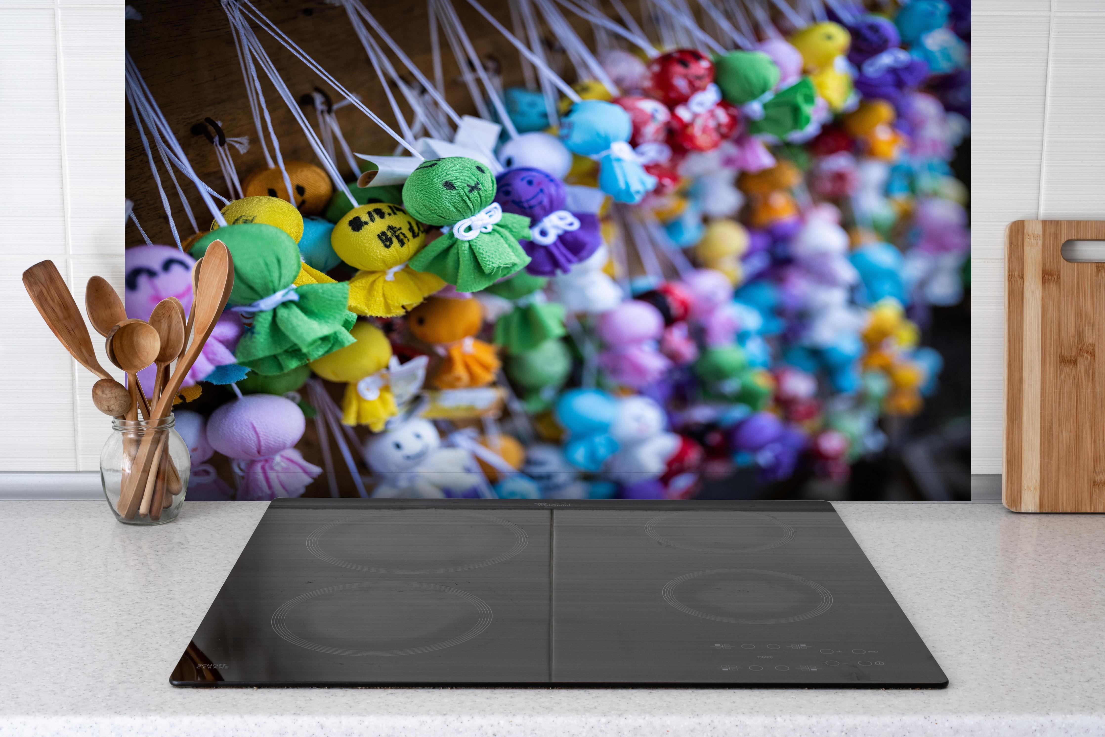 Spritzschutz - Bunte Glücksbringer hinter einem Cerankochfeld zwischen Holz-Kochutensilien