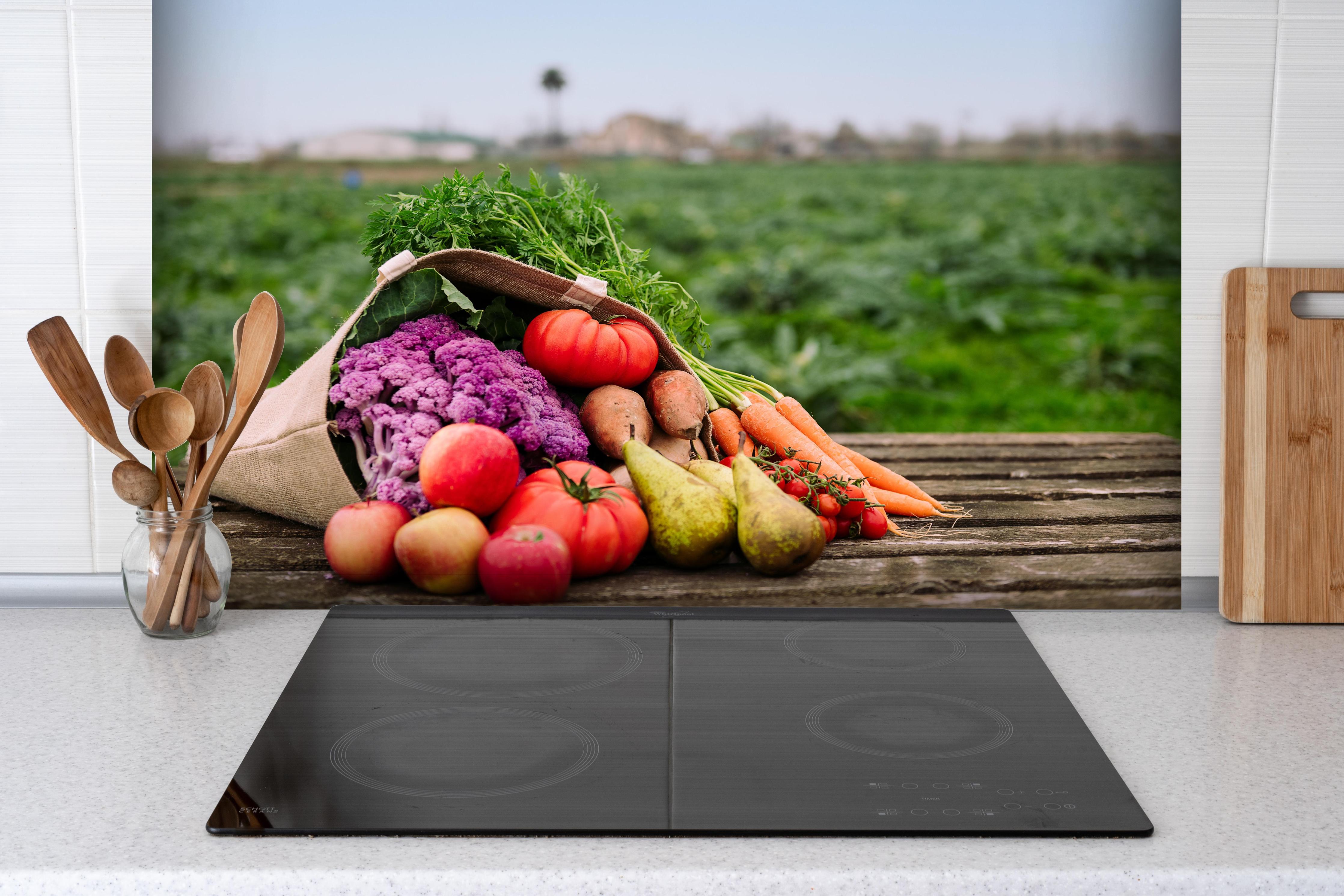 Spritzschutz - Bunte Vielfalt frischer Bio-Ernte hinter einem Cerankochfeld zwischen Holz-Kochutensilien