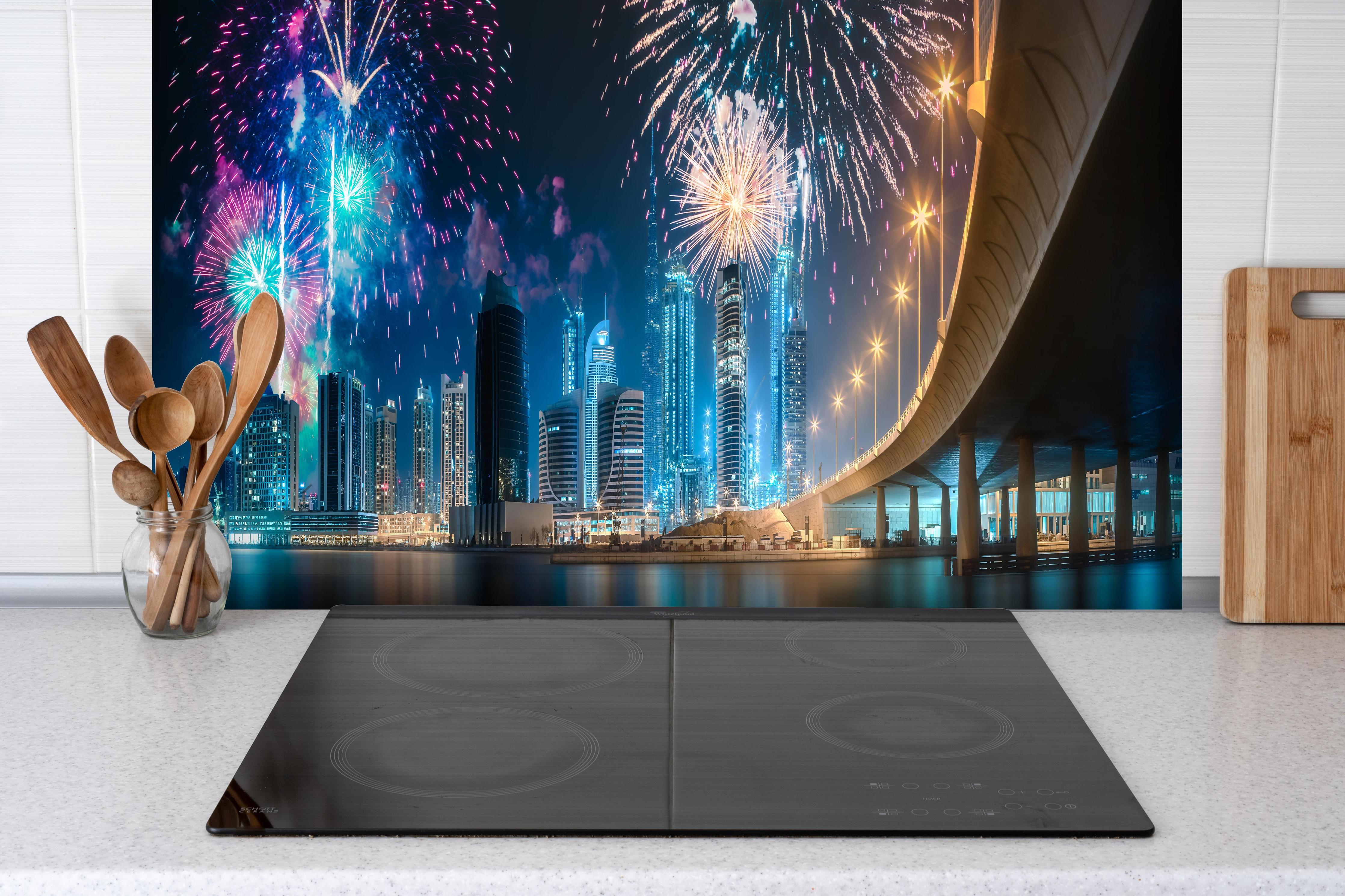 Spritzschutz - Buntes Feuerwerk über Dubai Business Bay hinter einem Cerankochfeld zwischen Holz-Kochutensilien