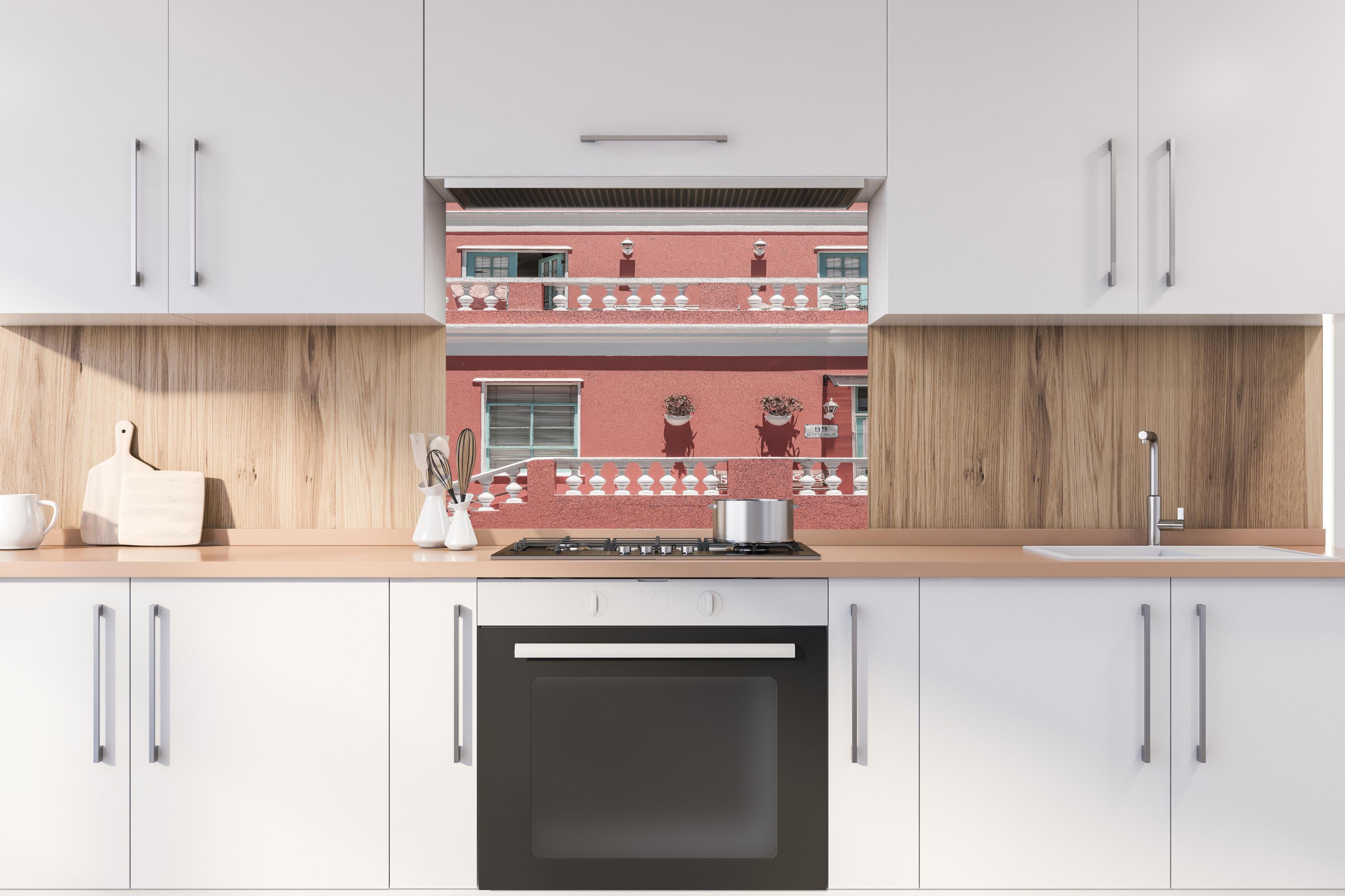 Spritzschutz - Buntes Gebäude mit pinker Fassade hinter einem Cerankochfeld zwischen Holz-Kochutensilien