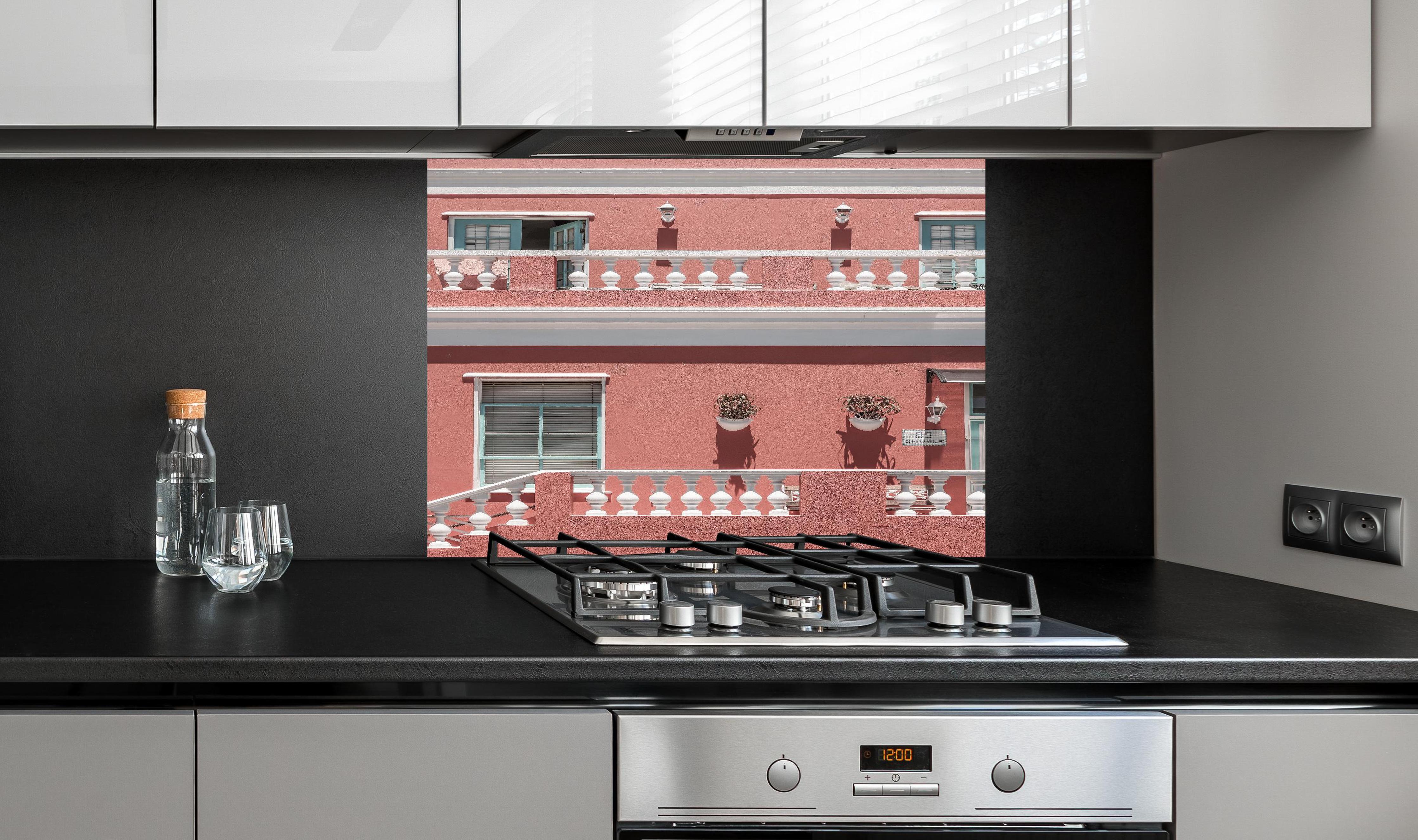 Spritzschutz - Buntes Gebäude mit pinker Fassade hinter einem Cerankochfeld zwischen Holz-Kochutensilien