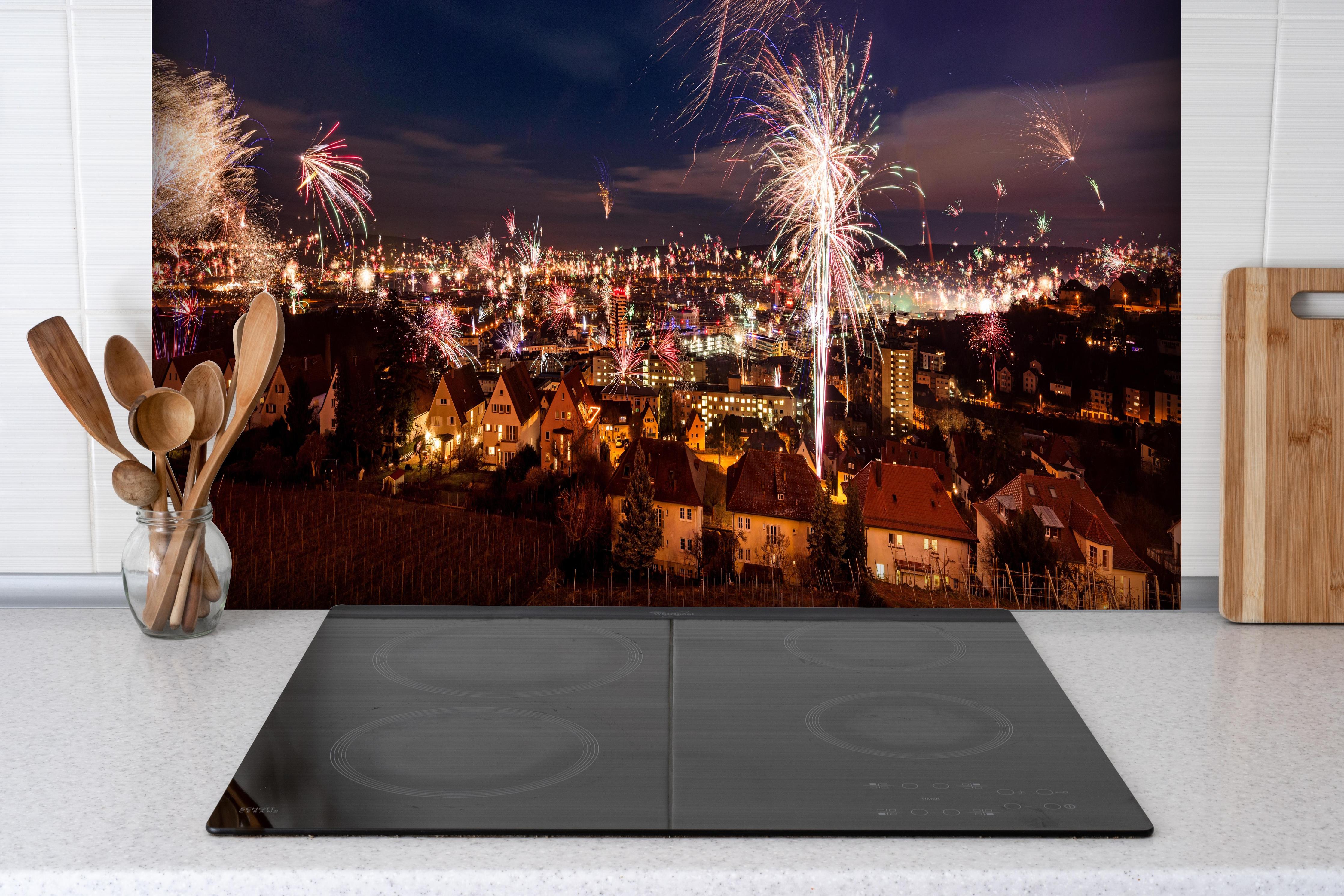 Spritzschutz - Buntes Neujahrsfeuerwerk über Stuttgart hinter einem Cerankochfeld zwischen Holz-Kochutensilien