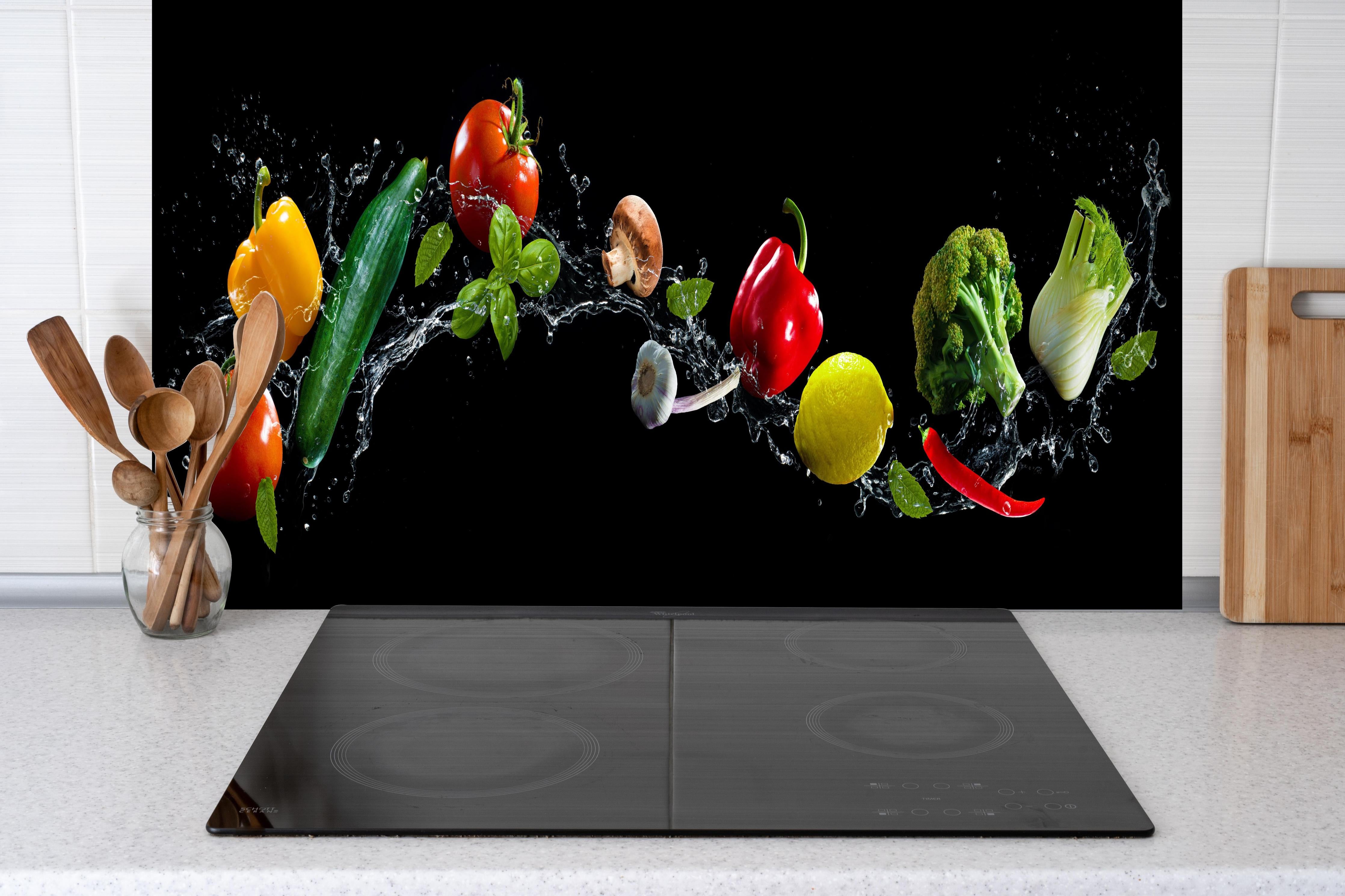 Spritzschutz - Buntes Spritzwasser-Gemüse auf Schwarz hinter einem Cerankochfeld zwischen Holz-Kochutensilien