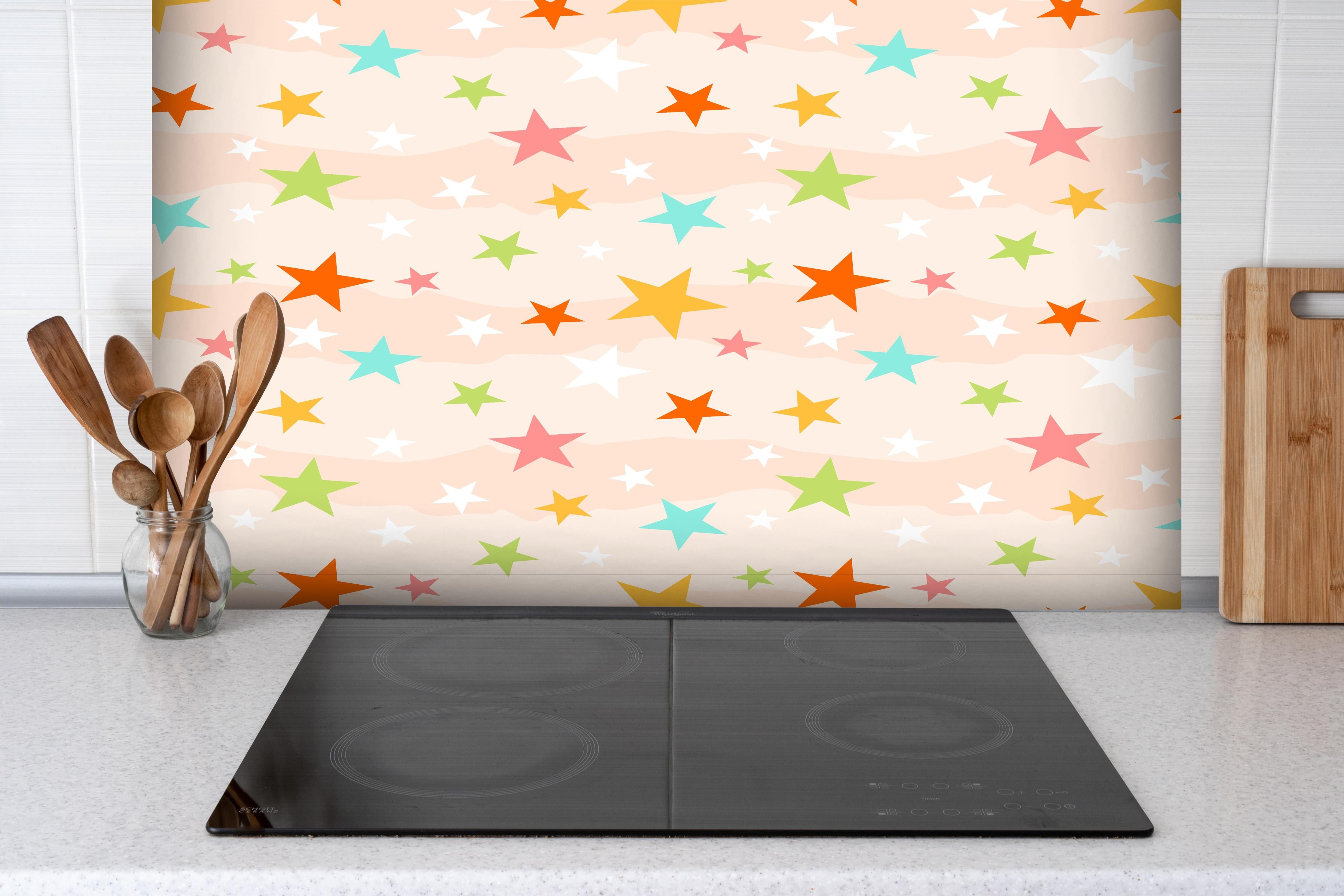 Spritzschutz - Buntes Sternmuster auf hellem Grund hinter einem Cerankochfeld zwischen Holz-Kochutensilien