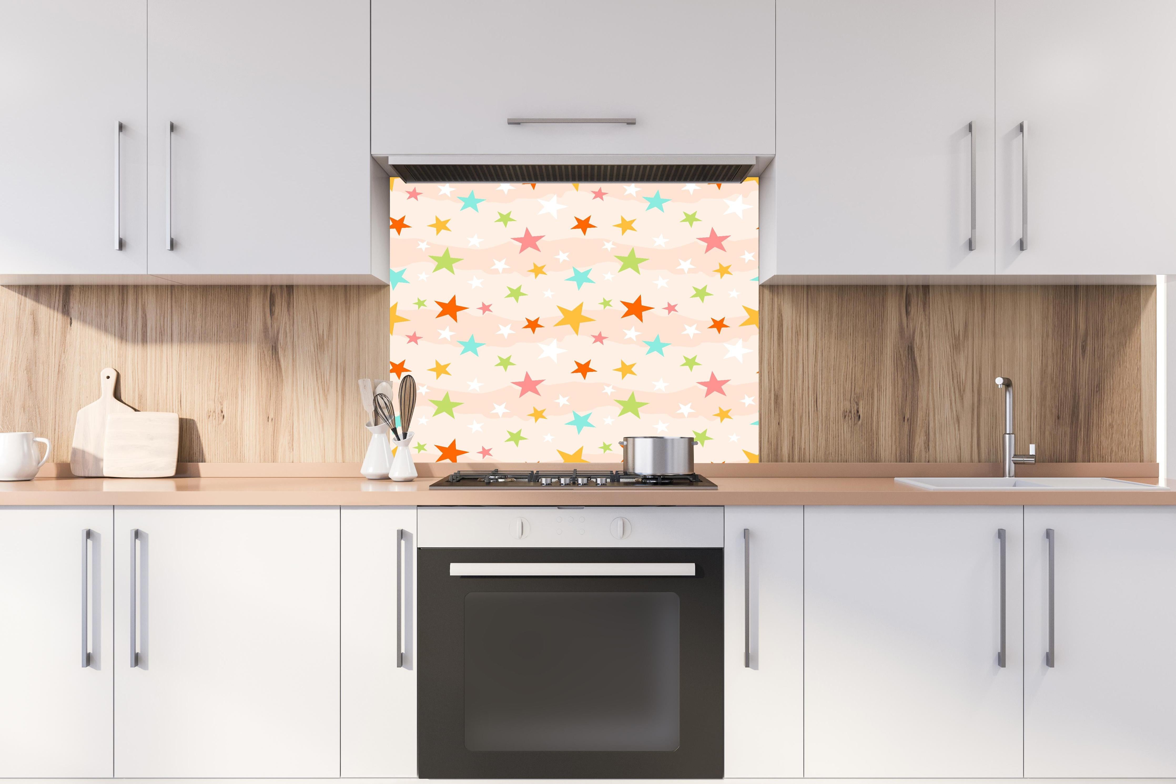 Spritzschutz - Buntes Sternmuster auf hellem Grund hinter einem Cerankochfeld zwischen Holz-Kochutensilien