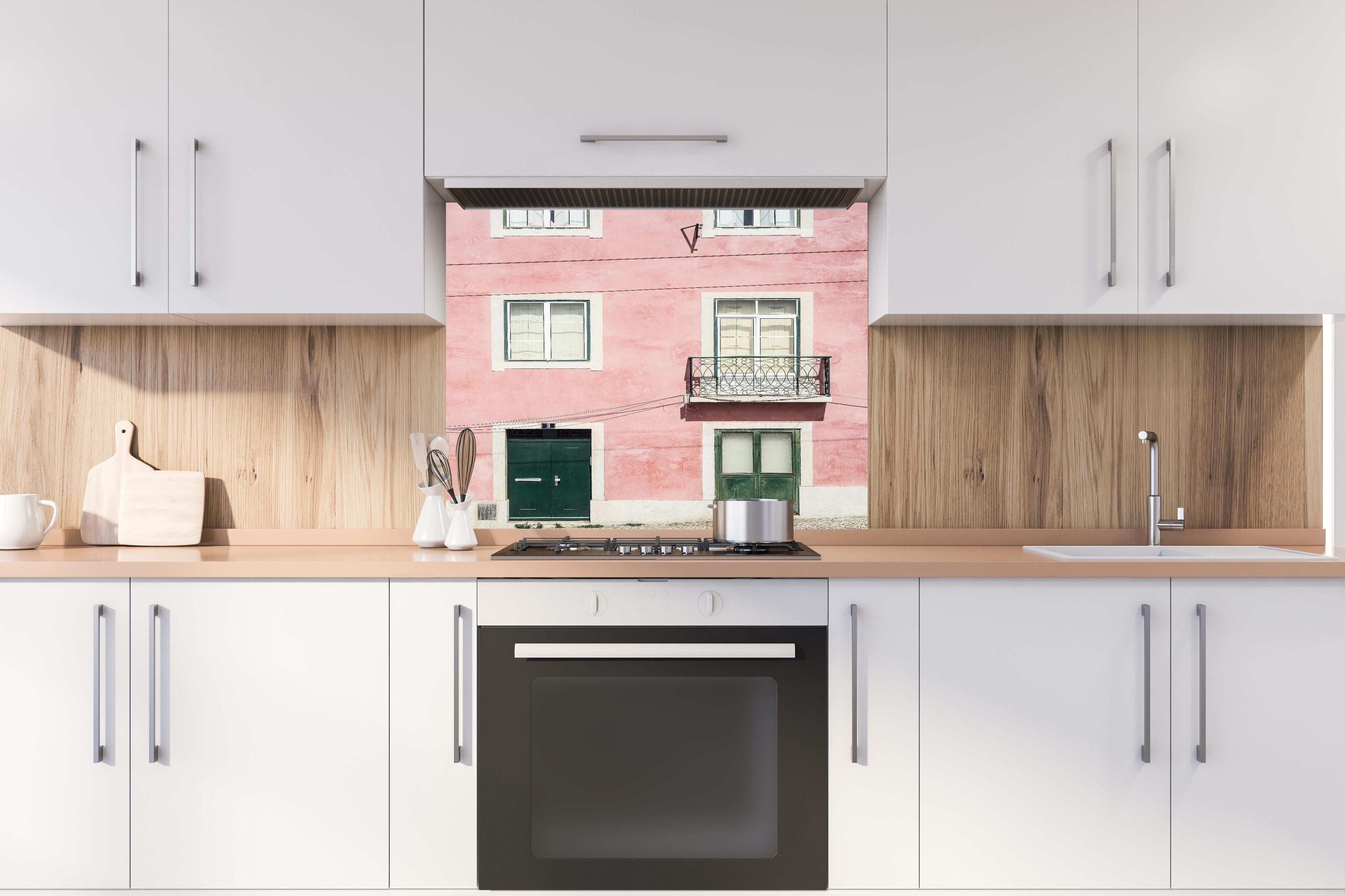 Spritzschutz - Charmante Pastellrosa Fassade mit Balkon hinter einem Cerankochfeld zwischen Holz-Kochutensilien