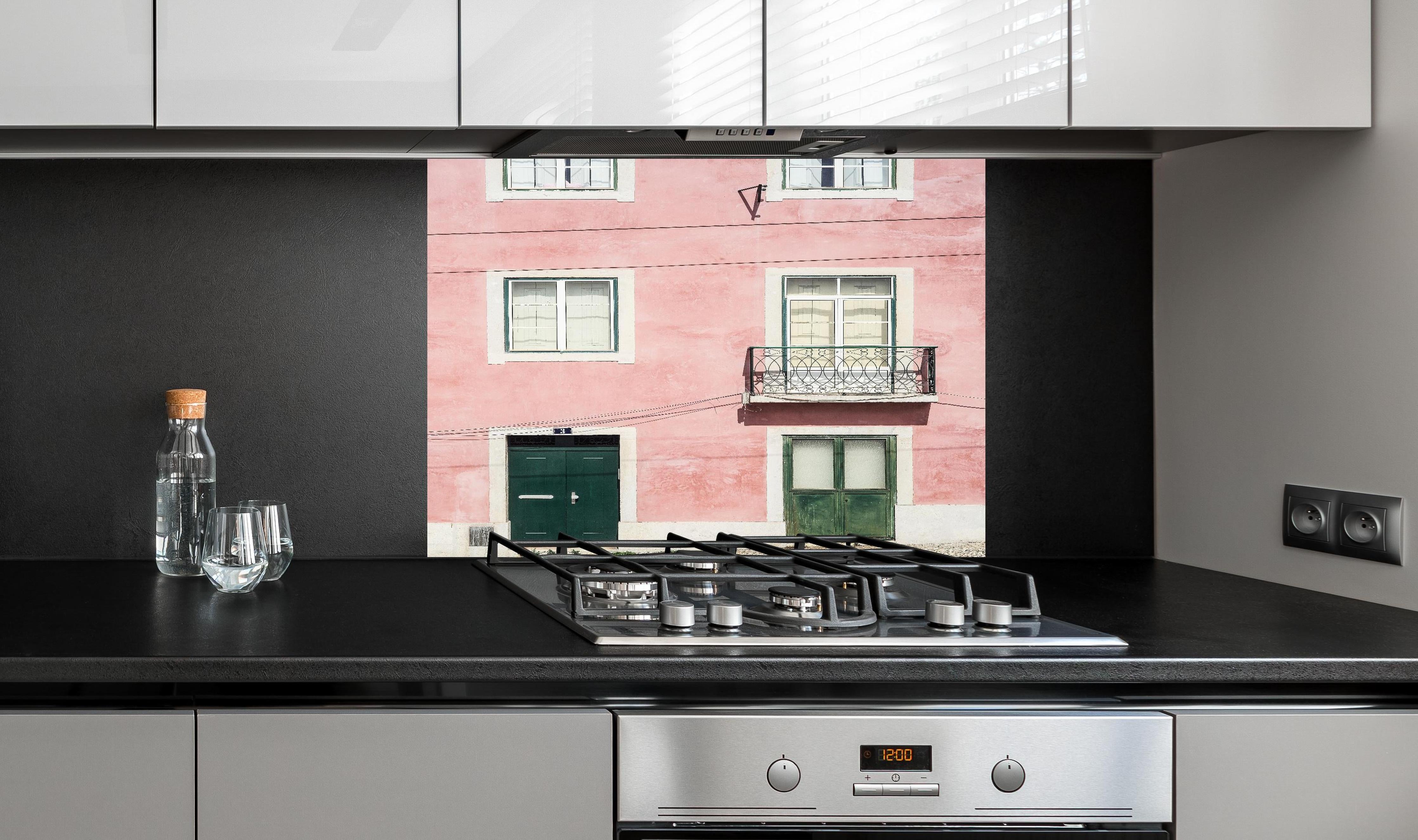 Spritzschutz - Charmante Pastellrosa Fassade mit Balkon hinter einem Cerankochfeld zwischen Holz-Kochutensilien