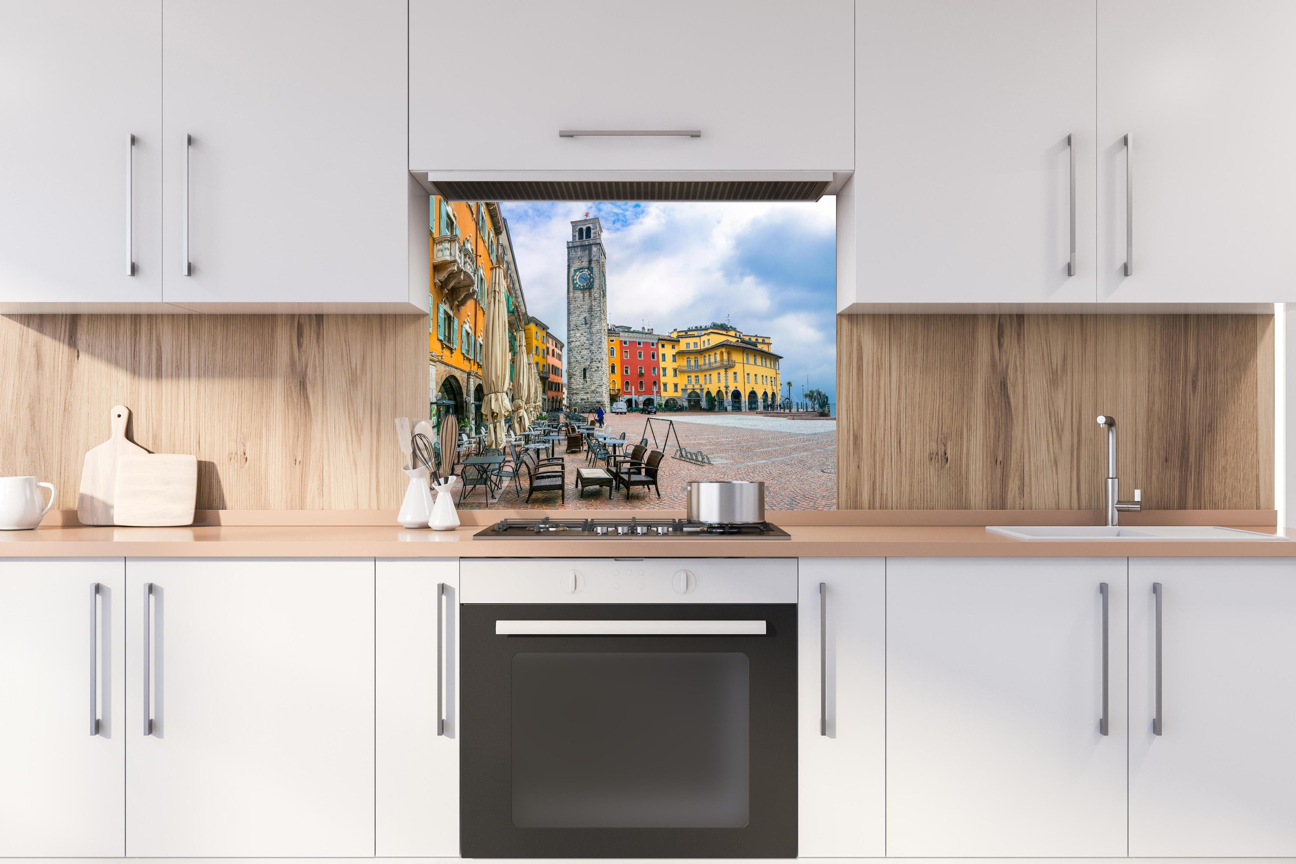 Spritzschutz - Charmante Stadt am Gardasee - Riva del Garda hinter einem Cerankochfeld zwischen Holz-Kochutensilien