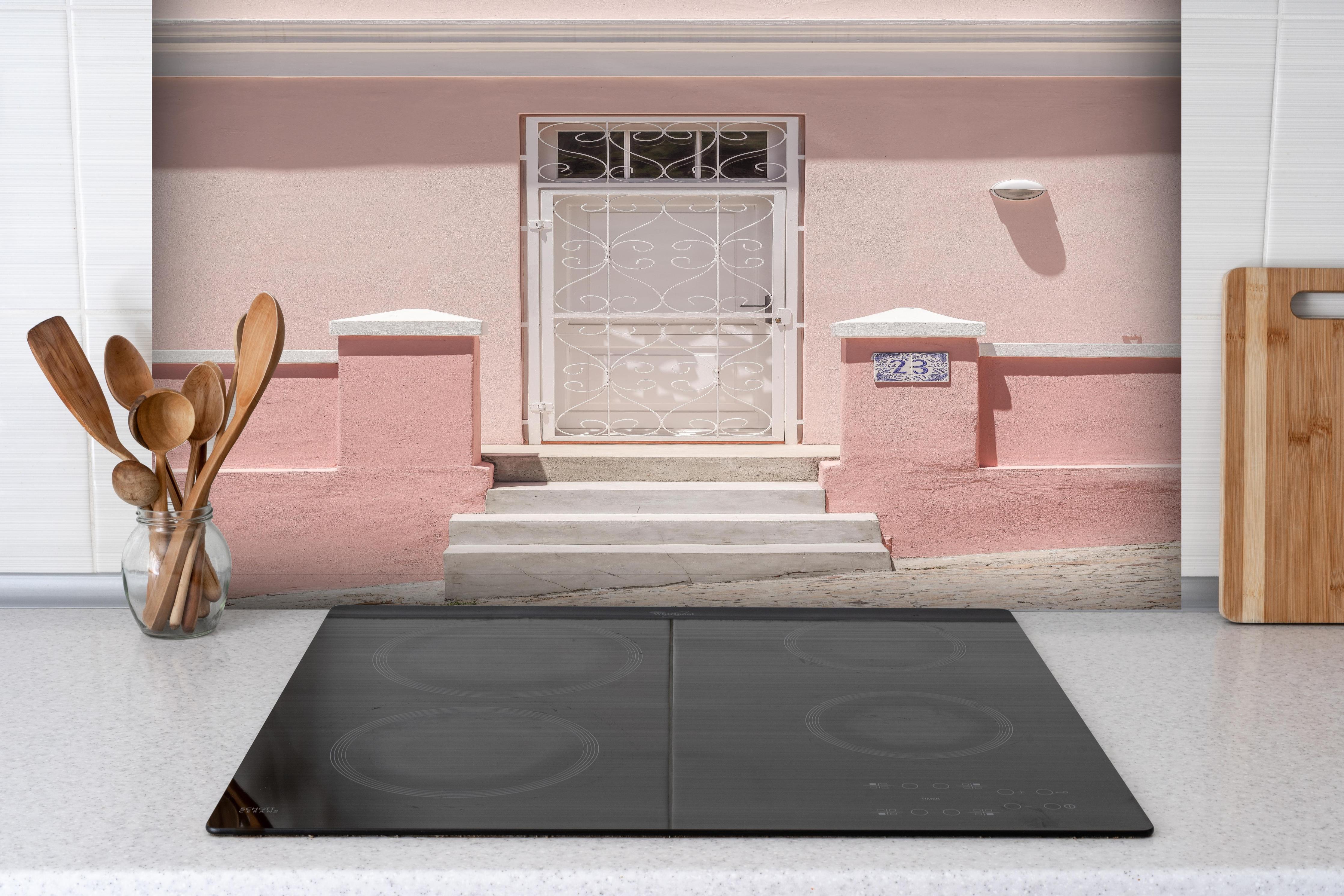 Spritzschutz - Charmante pastellrosa Hausfassade hinter einem Cerankochfeld zwischen Holz-Kochutensilien